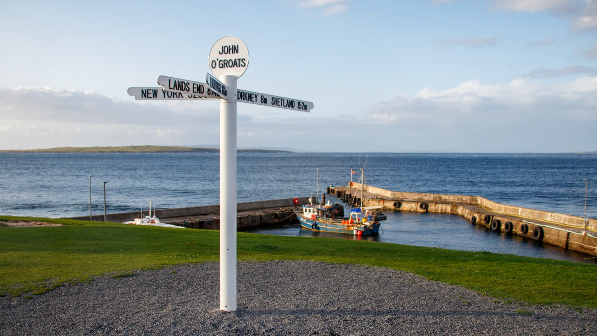 Sign post at John O'Groats with fishing boats in the background