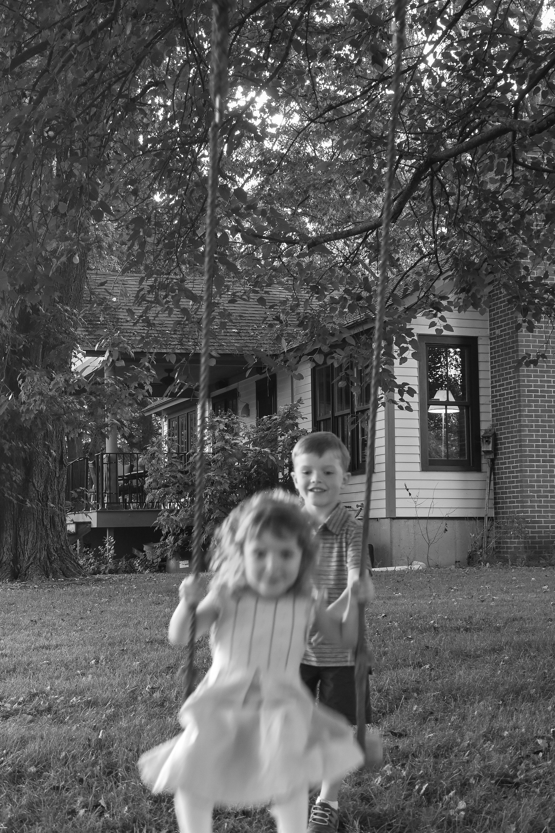 Two children play on a tree swing during playful family portraits in front of their grandparents' home at dusk during a family portrait session with photographer Lauren Nikiel Studio, a North Carolina (NC) photographer.