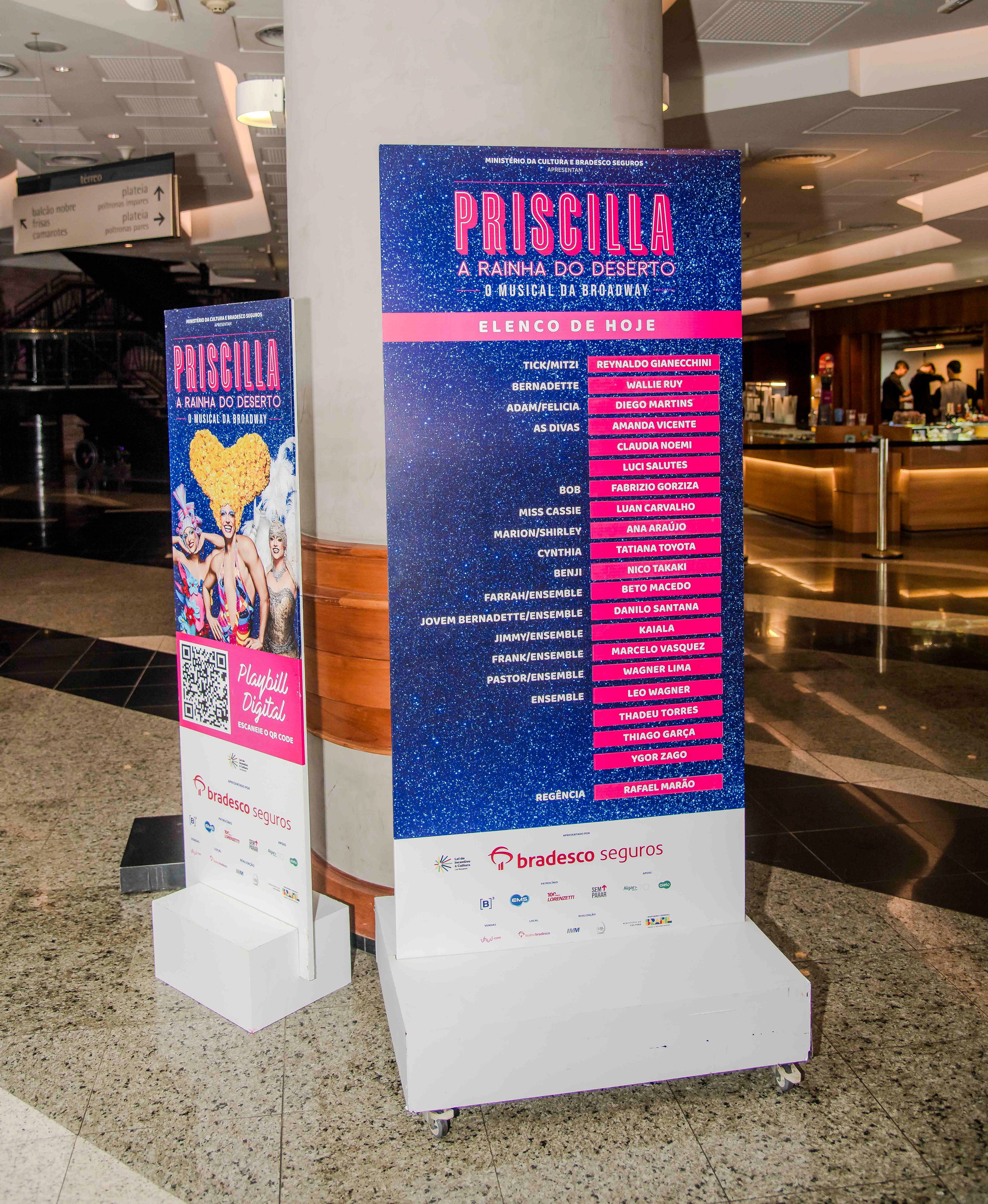 Info totems inside the Bradesco Theater foyer. Left: QR code to access the digital playbill. Right: list of the day's cast.
