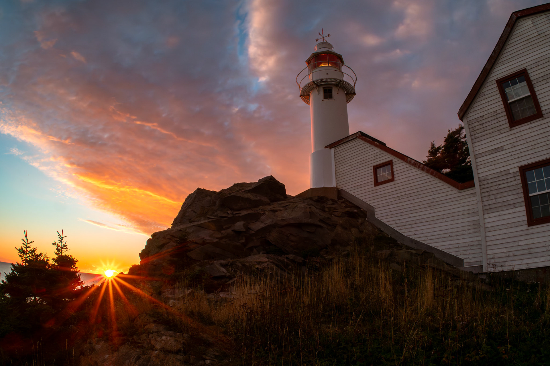 Golden hour at Lobster Cove Lighthouse, Gros Morne National Park – where the sun dips below the horizon, casting a fiery glow against the rugged coastline. The lighthouse stands tall, a timeless guardian of the sea, as the sky ignites with hues of orange, pink, and blue. A perfect moment of serenity on Newfoundland’s breathtaking west coast.