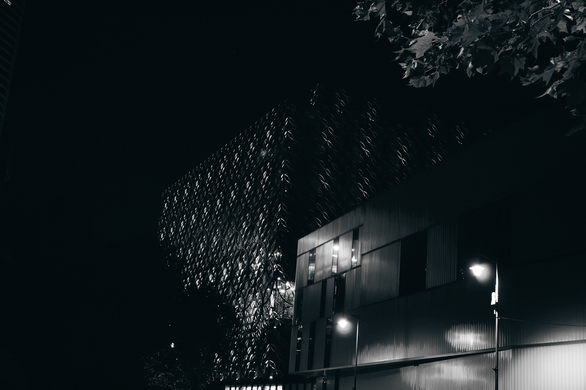 A black and white photo of birmingham library lit up at night with the back of the rep theatre next to it.
