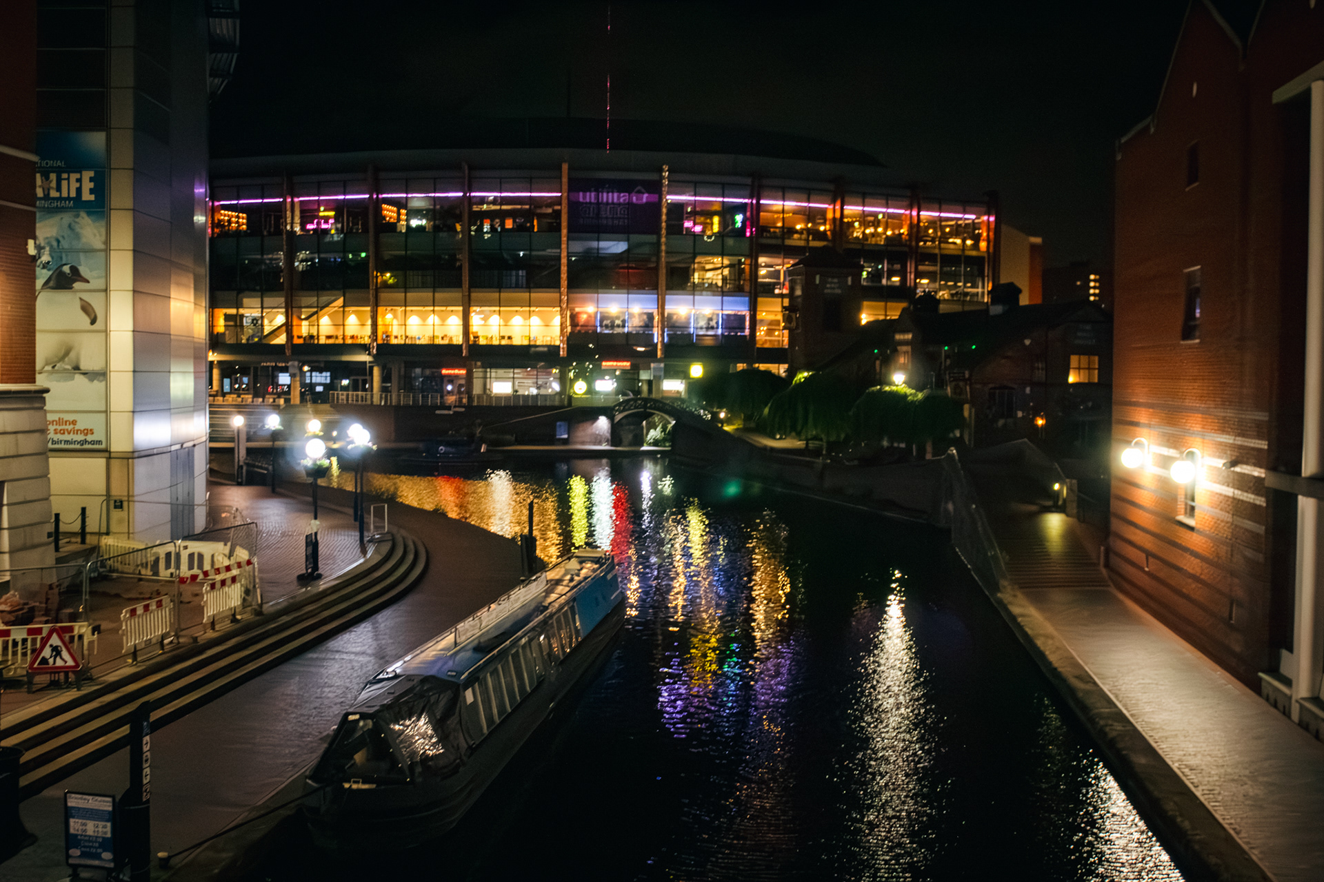 A night time shot of a lit up glass building with the canal infront of it reflecting the lights.