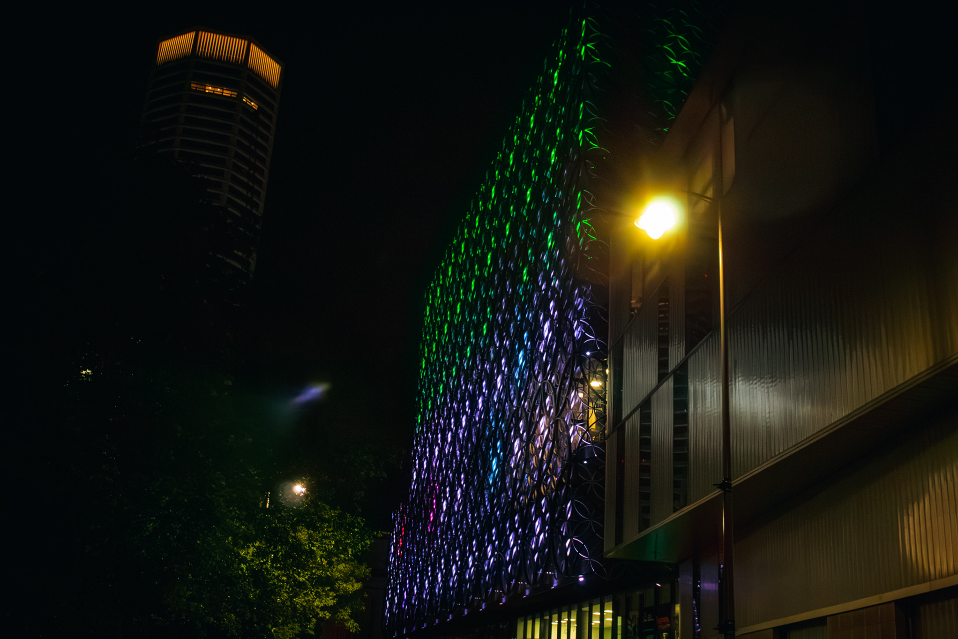 A photo of birmingham library lit up at night in purple and green with the octagon building on the left side of the screen.