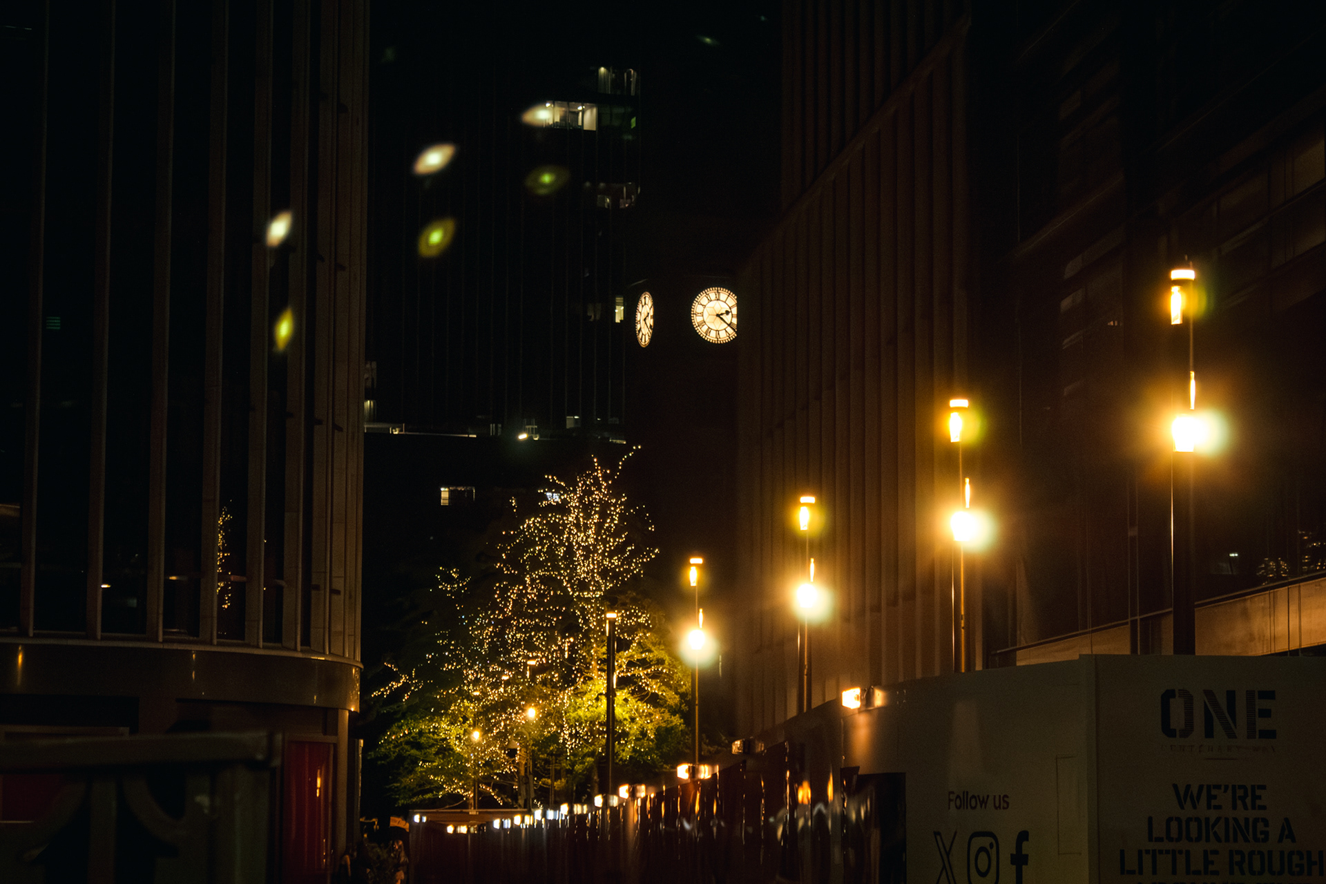 A photo of a clock with street lights and lit up trees.