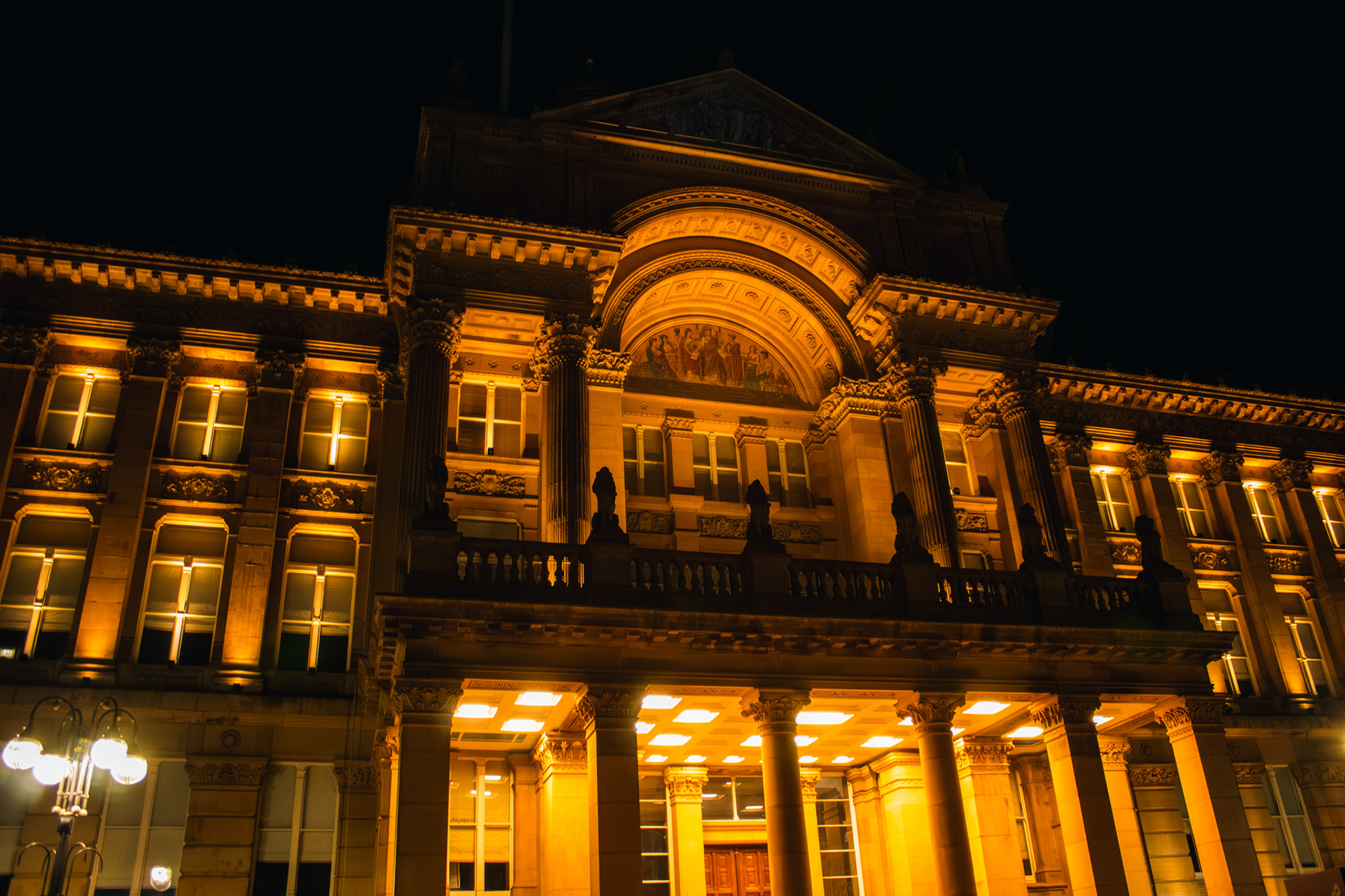 A photo of birmingham council house lit up in a gloden light at night.