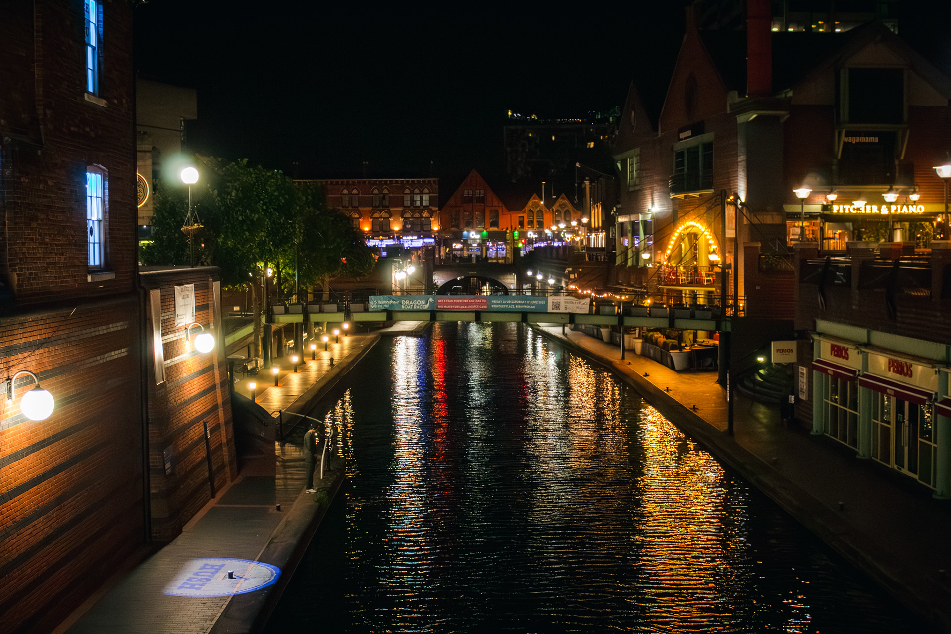 A night time shot of building along the right side of the canal with the lights from them reflecting into the water.