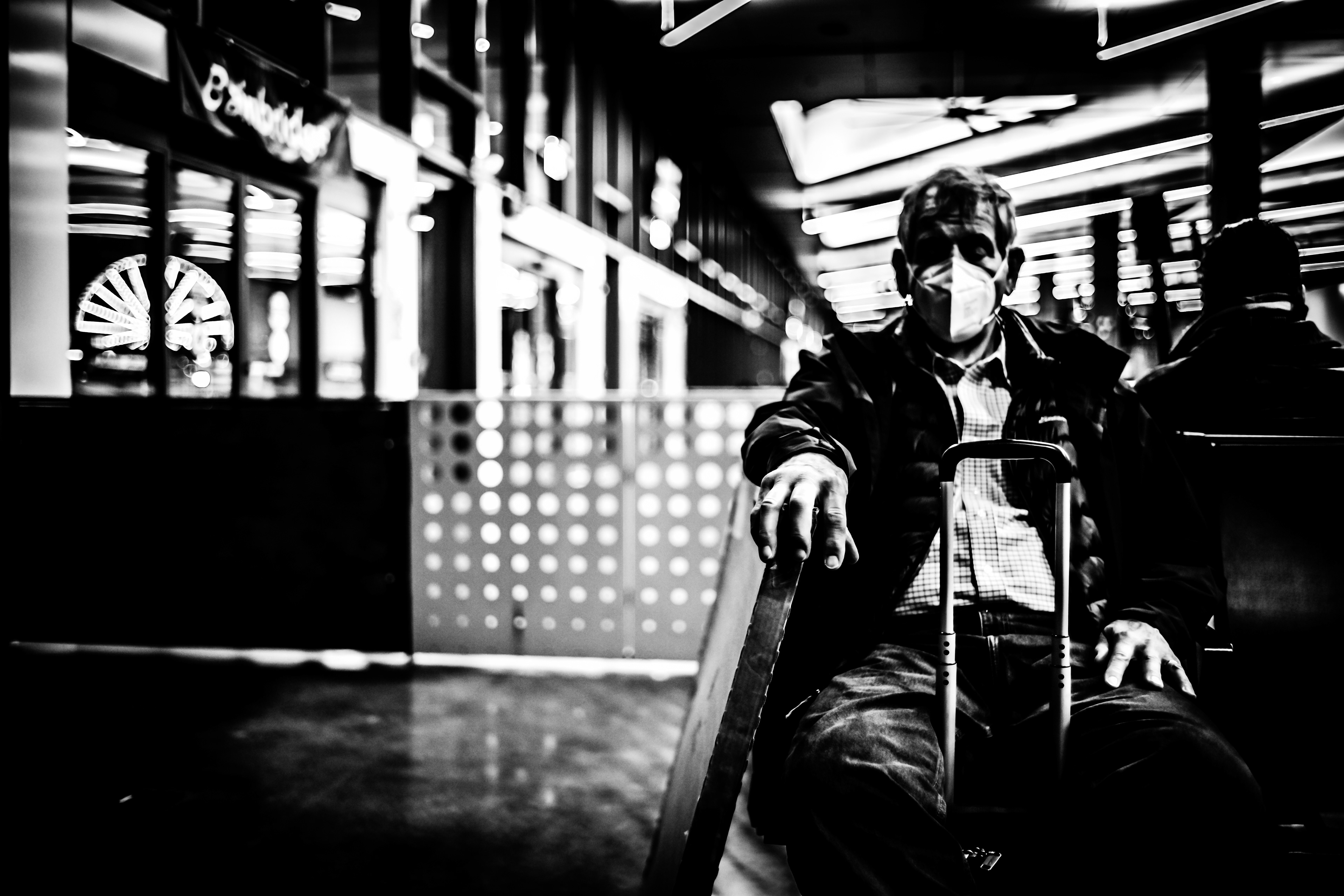 An elder man on a surgical mask takes a nap while waiting for a ferry. A ferris wheel is at the background facing out of the window terminal in seattle.