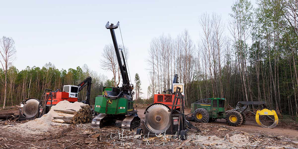 Photo of four forest harvesting machines prior to light painting them. There's a SERCO 300 Series Loader with a 72″ SERCO Saw, a John Deere 2154G Swing Machine with a Pro Pac Delimber, a second SERCO 300 Series Loader with a 72″ SERCO Saw. And, on the far right, a John Deere 948L-II Grapple Skidder.