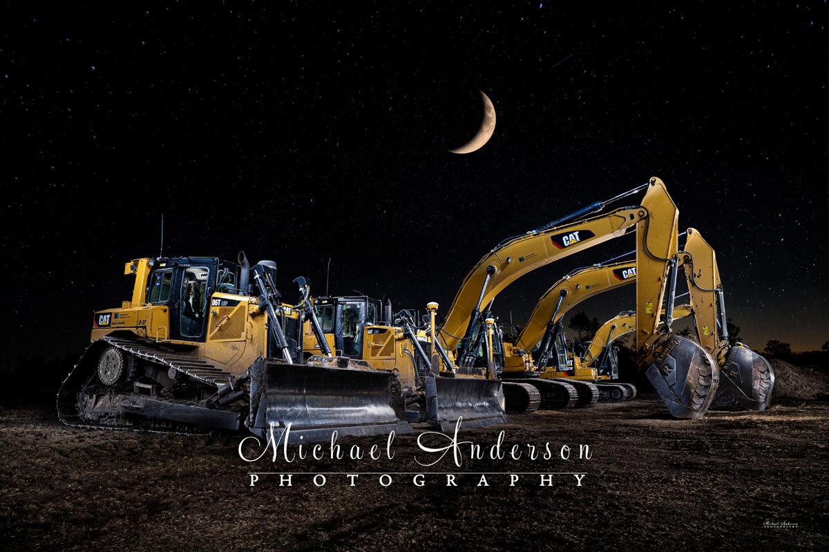 A cool light painted photo of five construction vehicles, 2 bulldozers, and 3 excavators, under a sky with a sliver of a moon. These rigs are owned and operated by North Pine Aggregate in Forest Lake, MN.