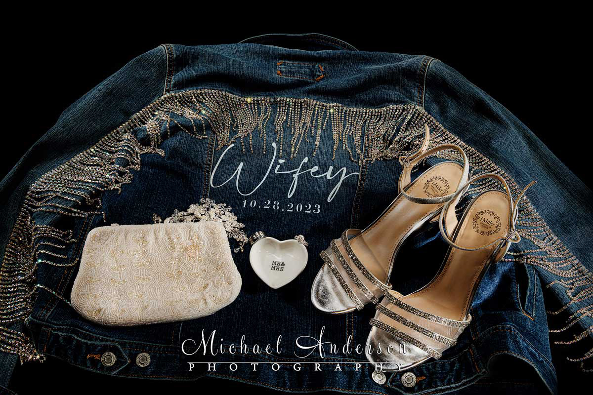 A pretty light painted wedding photograph of the bride's accessories. Her Jacket, purse, shoes, and their wedding rings are in the image.