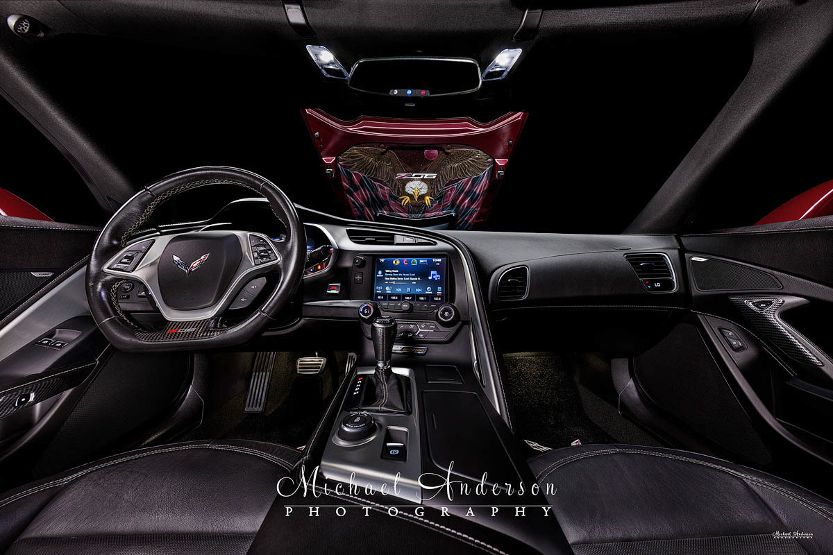 A cool light painted photograph of the interior of a 2016 C7 Corvette Z06. The custom, hand-painted hood liner featuring a bald eagle and a blood moon can be seen through he windshield.
