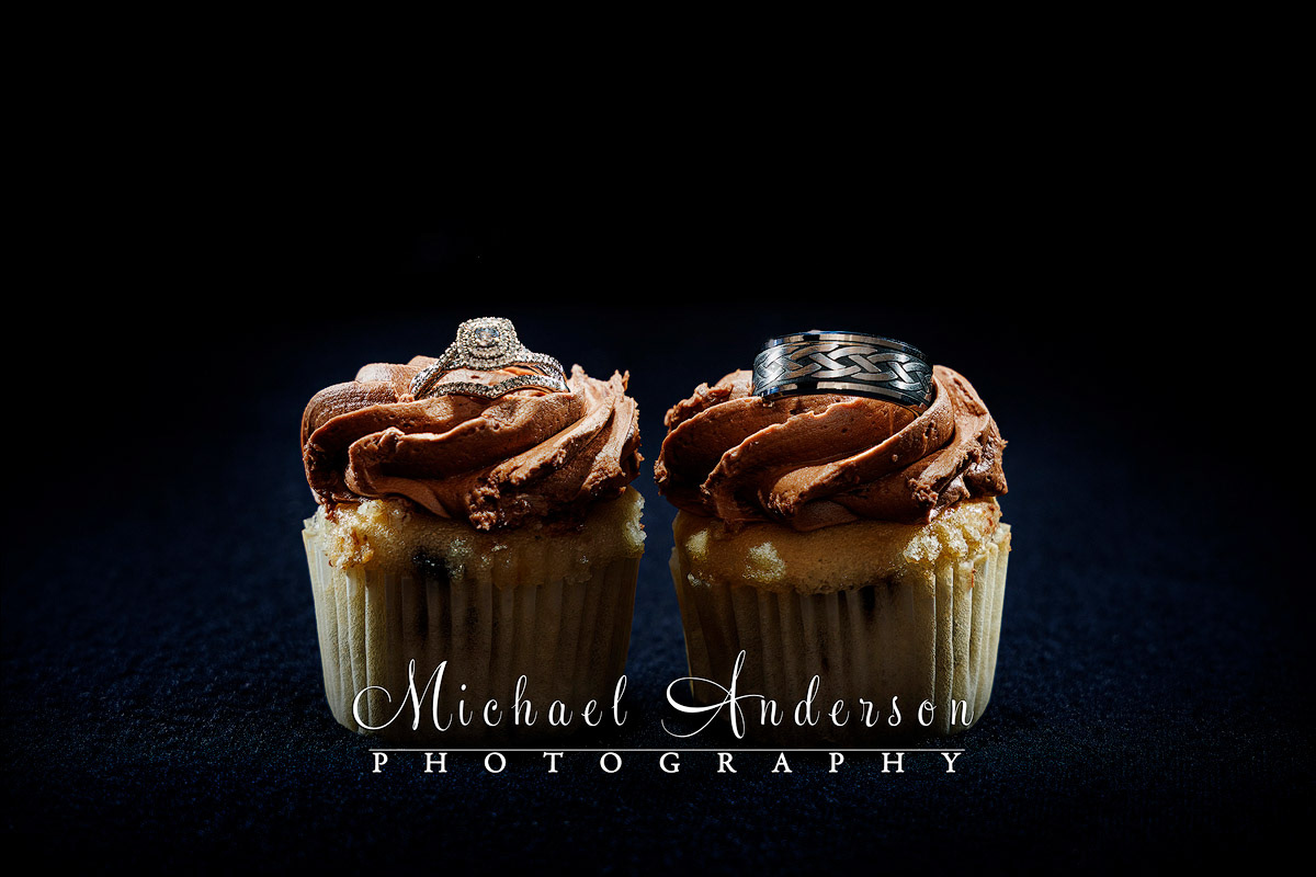 A cute light painted wedding photograph of the bride and grooms rings set in the frosting of a couple of cupcakes.