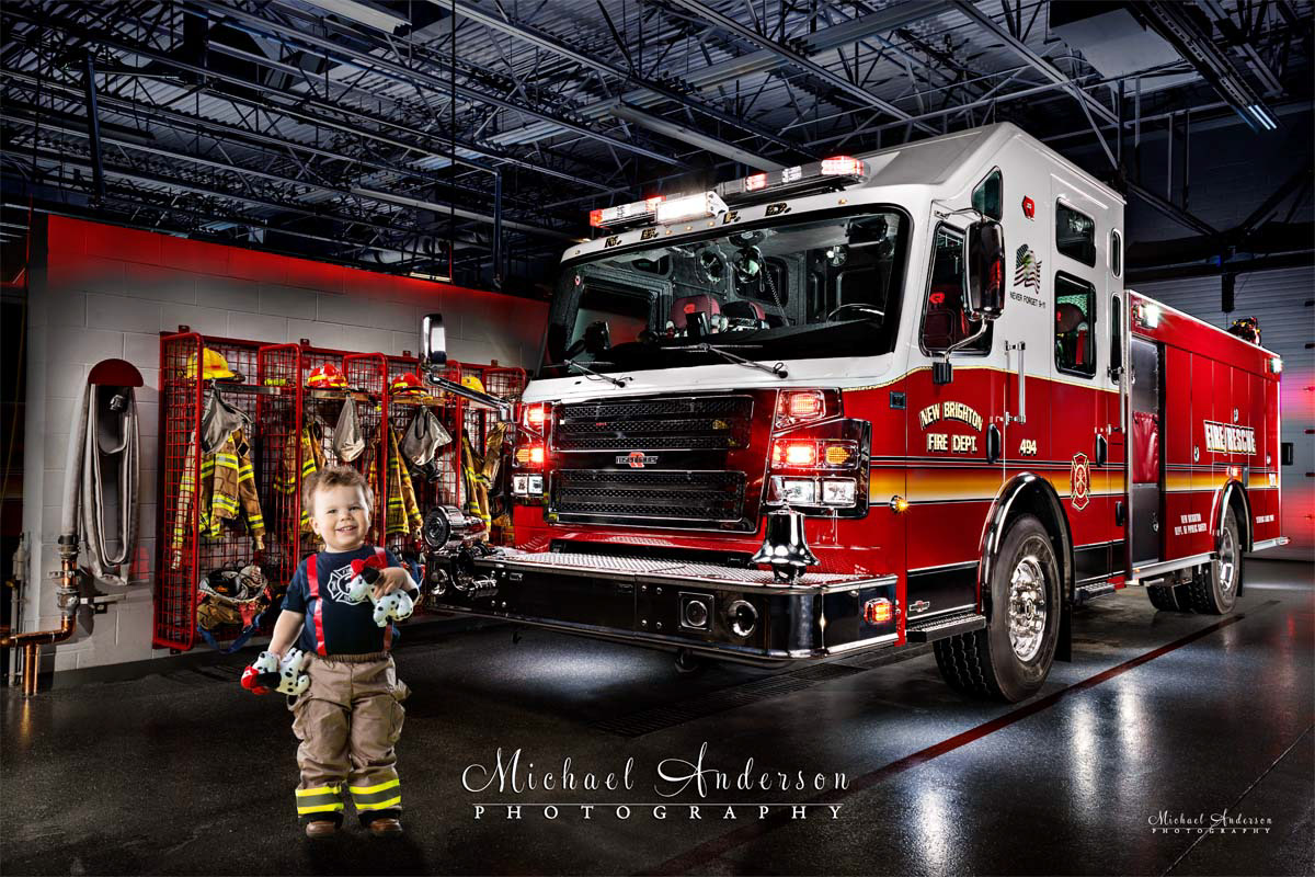 A cute light painted photo of a two-year-old boy holding two toy Dalmatian puppies in front of New Brighton Engine 494, created in the firehouse.