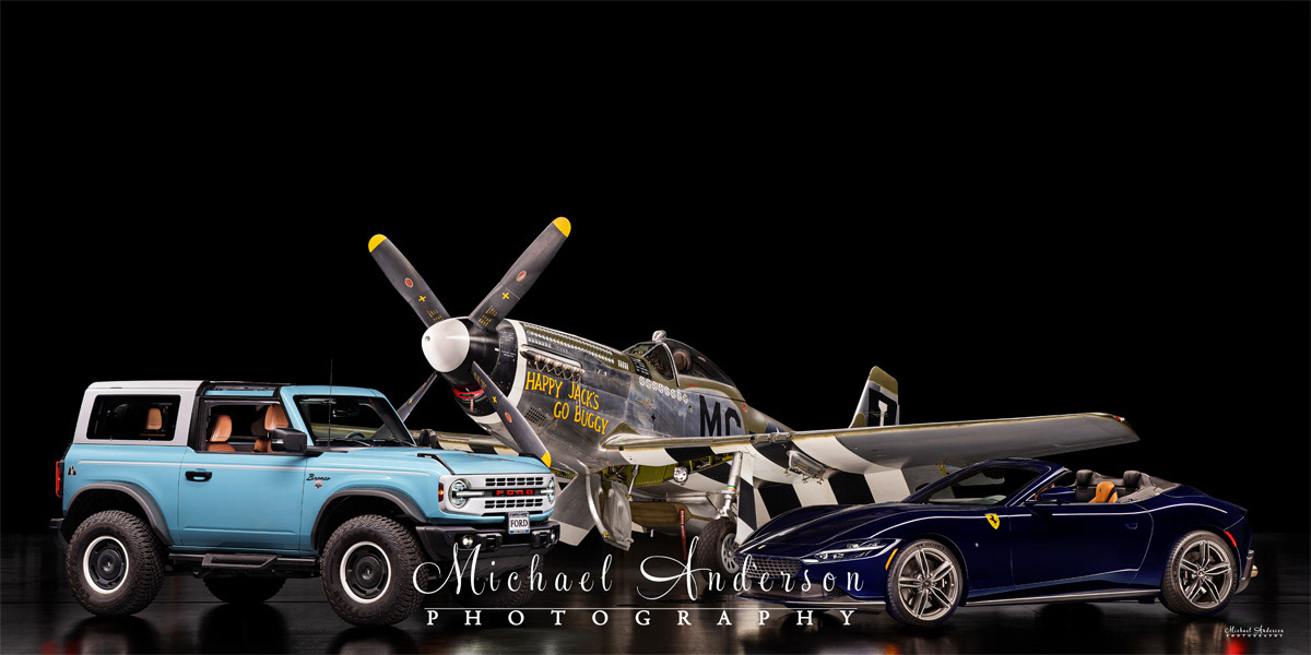 A stunning light-painted photograph of a 2024 Ford Bronco Heritage Edition, a 2025 Ferrari Roma Spider, and the P-51D Mustang, Happy Jack's Go Buggy!