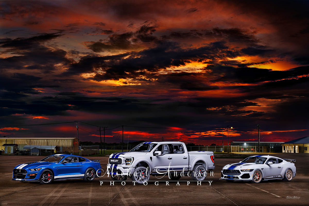 A cool light painted photograph of three Ford Shelbys. From left to right, we have a 2022 Ford Shelby GT500 Mustang, a 2022 Ford Shelby F-150 Truck Offroad Series, and a, 2024 Ford Shelby Super Snake Mustang.