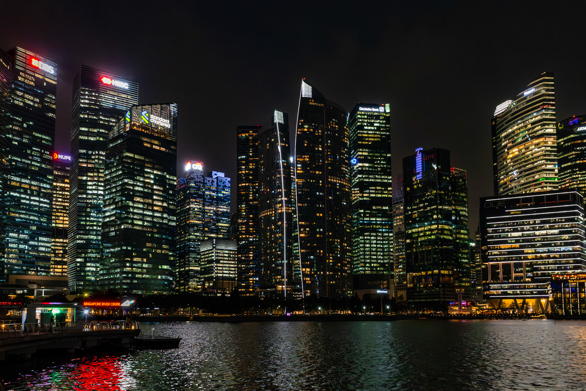 Skyline von Marina Bay bei Nacht mit Spiegelung im Wasser; Hochhäuser dicht gruppiert entlang der Bucht.