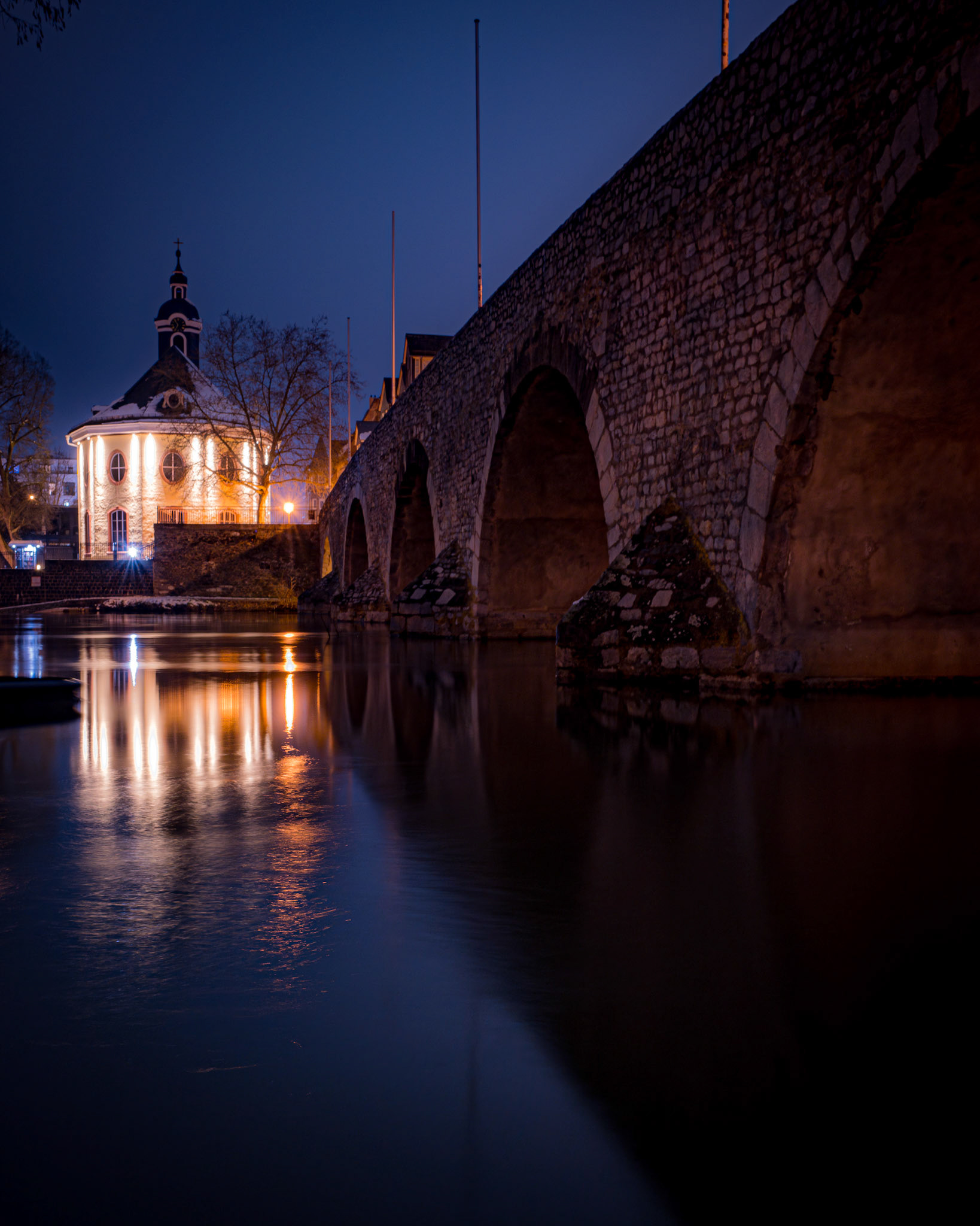Wehr, Hospitalkirche und Alte Lahnbrücke mit auf der Flussoberfläche reflektierenden Lichtern bei Nacht