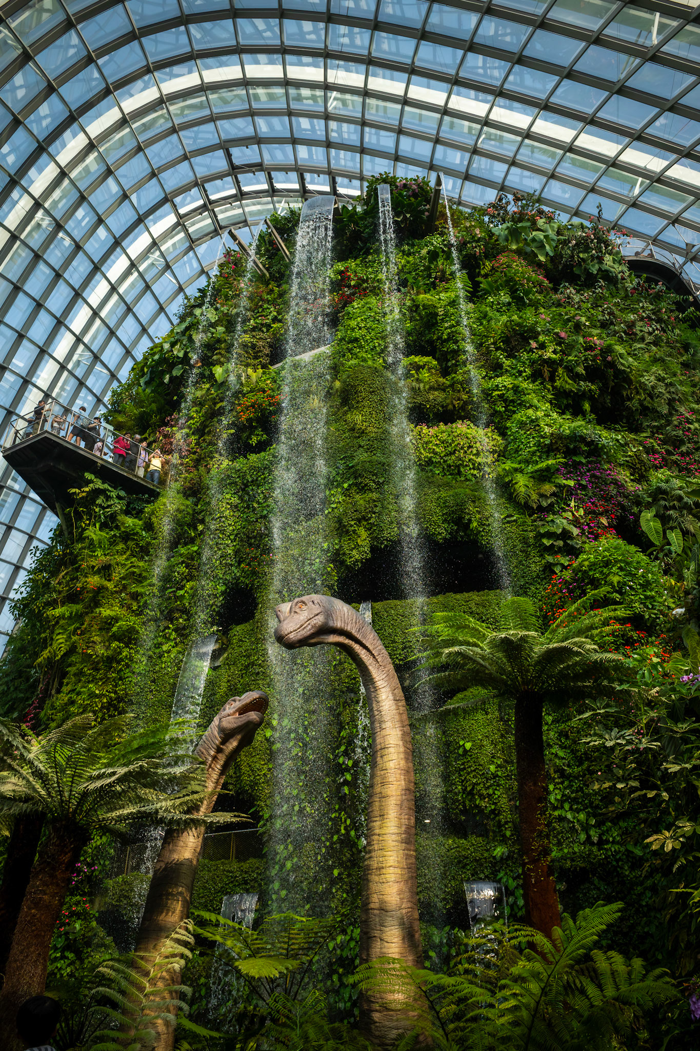 Gewächshaus mit tropischer Vegetation und Glasstruktur; hohe Pflanzen wachsen unter der gewölbten Konstruktion.