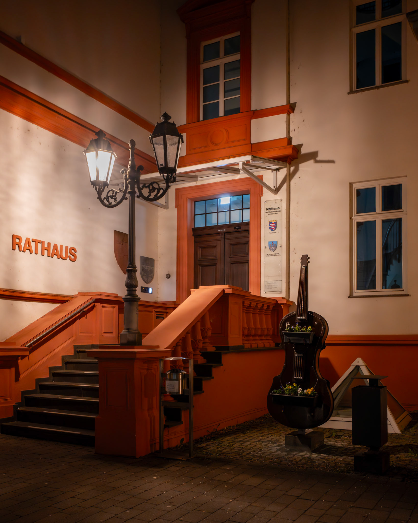 Man beachte die halbfunktionale Straßenlampe und das dekorative Cello, umringt von Mülleimer und Aschenbecher