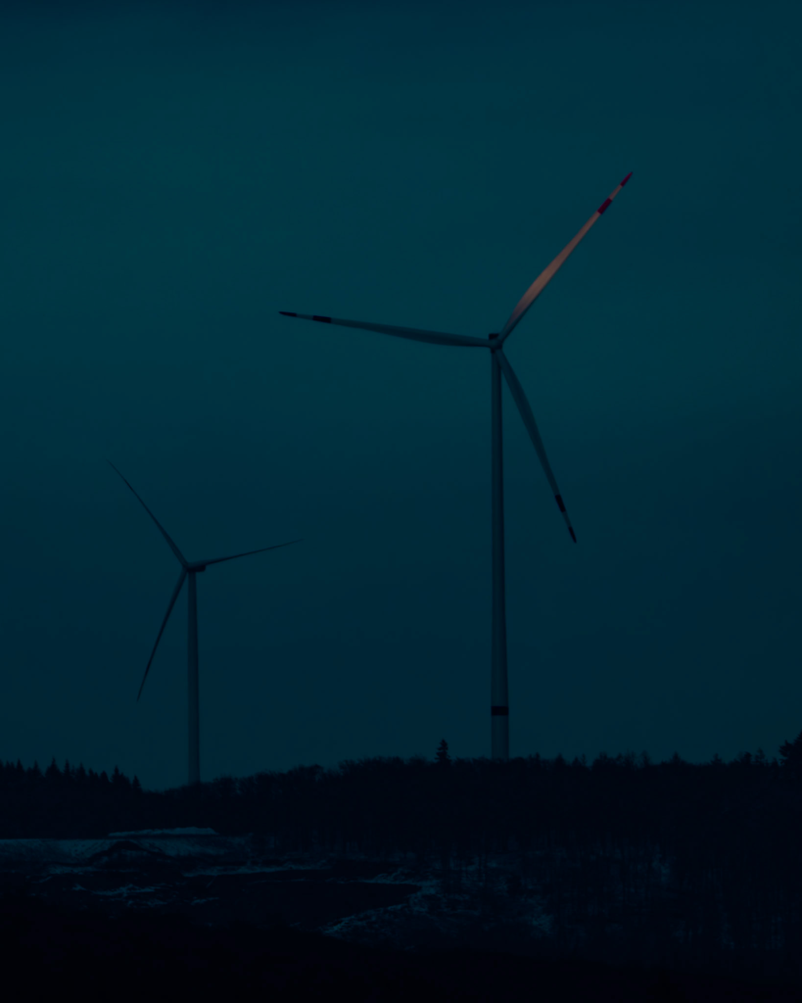 Windräder im Westerwald mit einem Rotorblatt im letzten Sonnenlicht