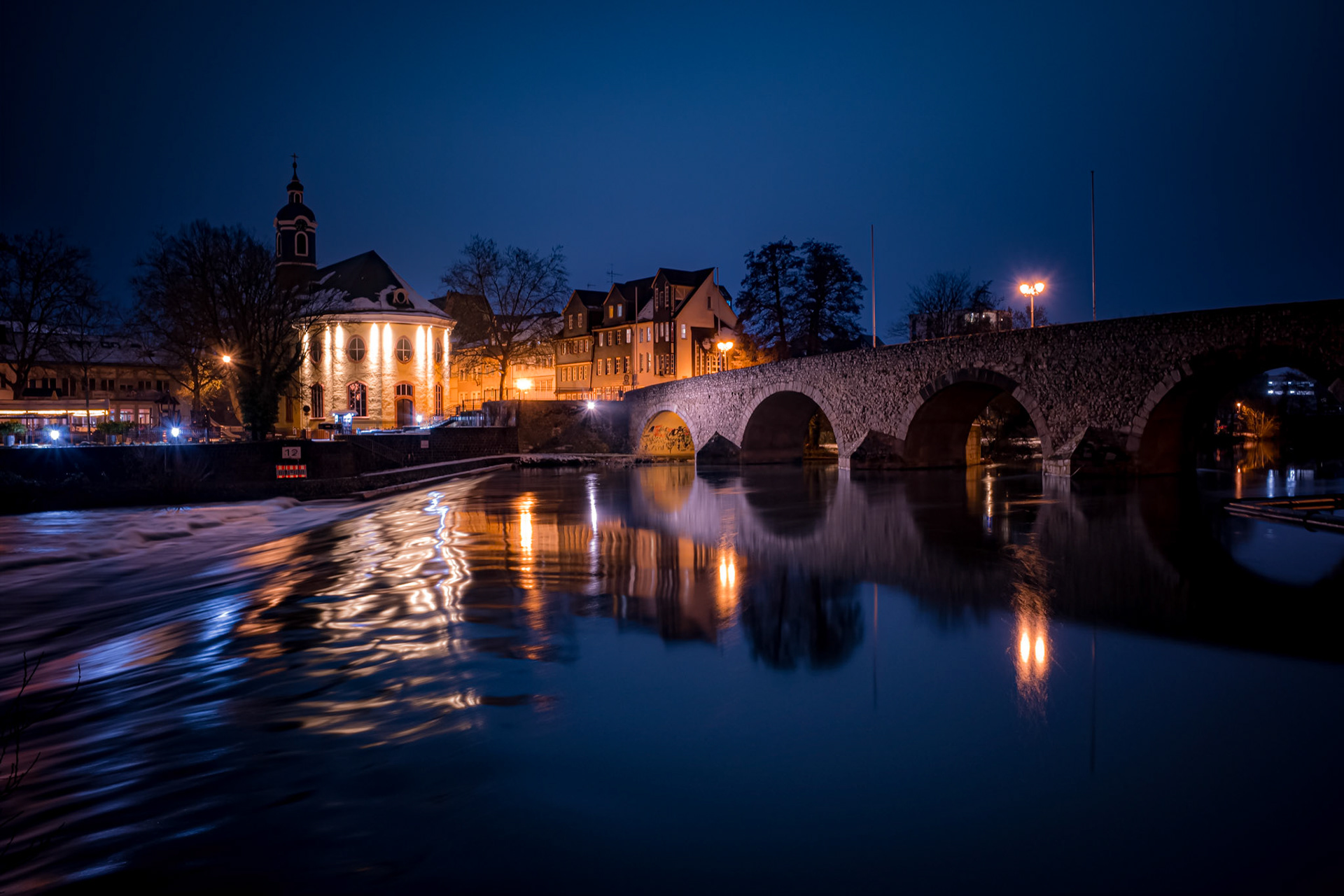 Wehr, Hospitalkirche und Alte Lahnbrücke mit auf der Flussoberfläche reflektierenden Lichtern bei Nacht