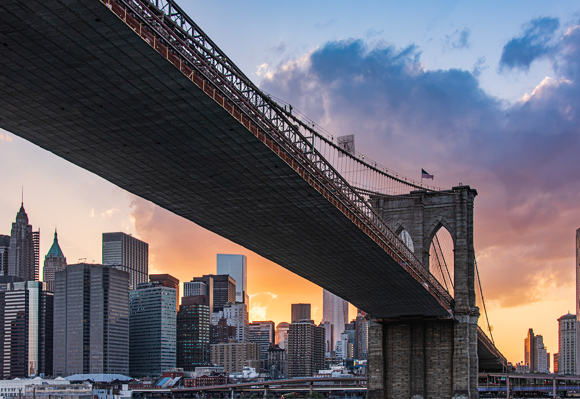 The Brooklyn Bridge is a hybrid cable-stayed/suspension bridge in New York City and is one of the oldest bridges of either type in the United States. Completed in 1883, it connects the boroughs of Manhattan and Brooklyn by spanning the East River.