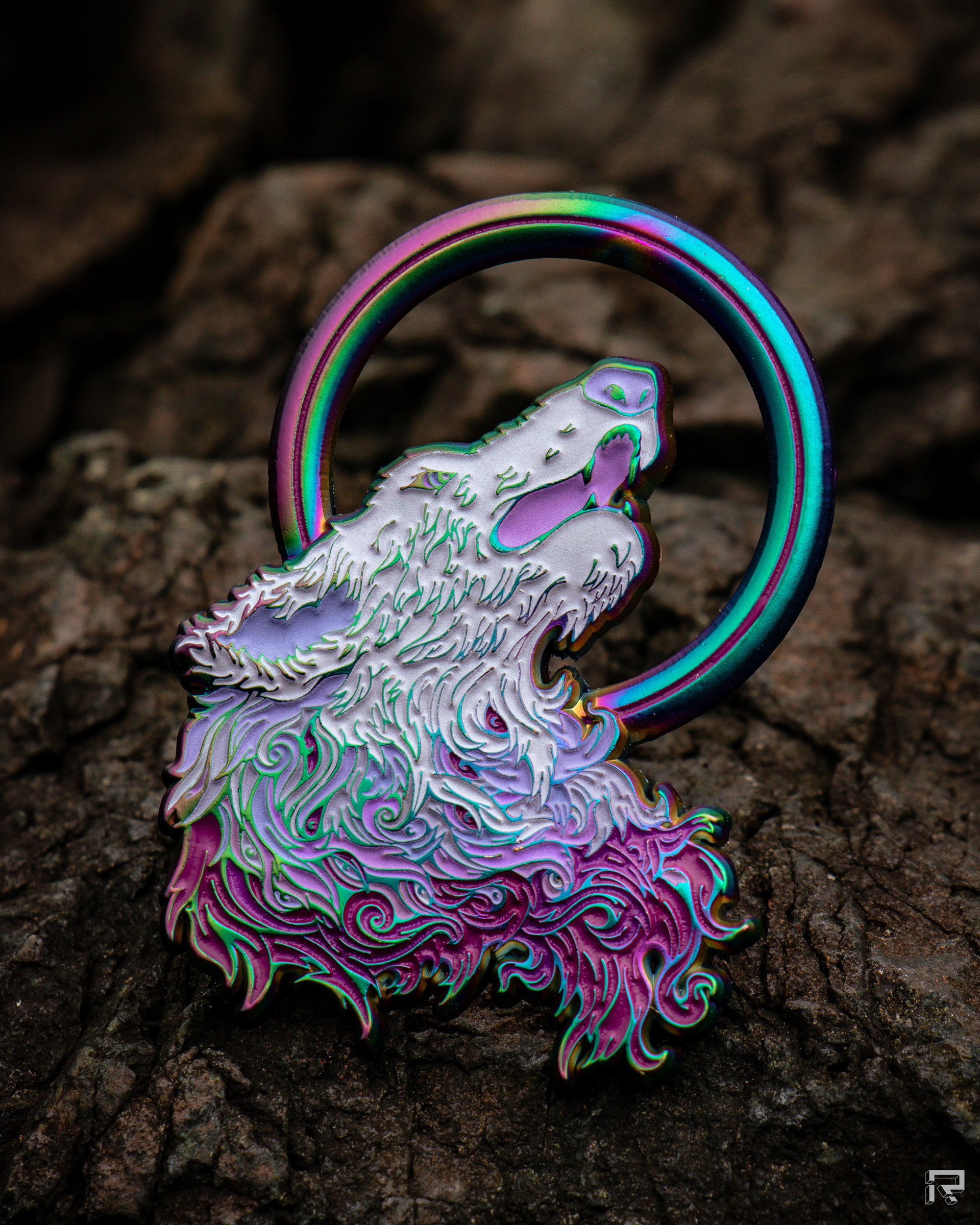 Enamel pin featuring artwork of a wolf's head howling at a ring-shaped moon. The wolf's fur undulates with a flame-like quality, the line work is highly detailed. The wolf's head is very light purple, and the colors transition to the neck area to maroon. The pin is made of rainbow metal.