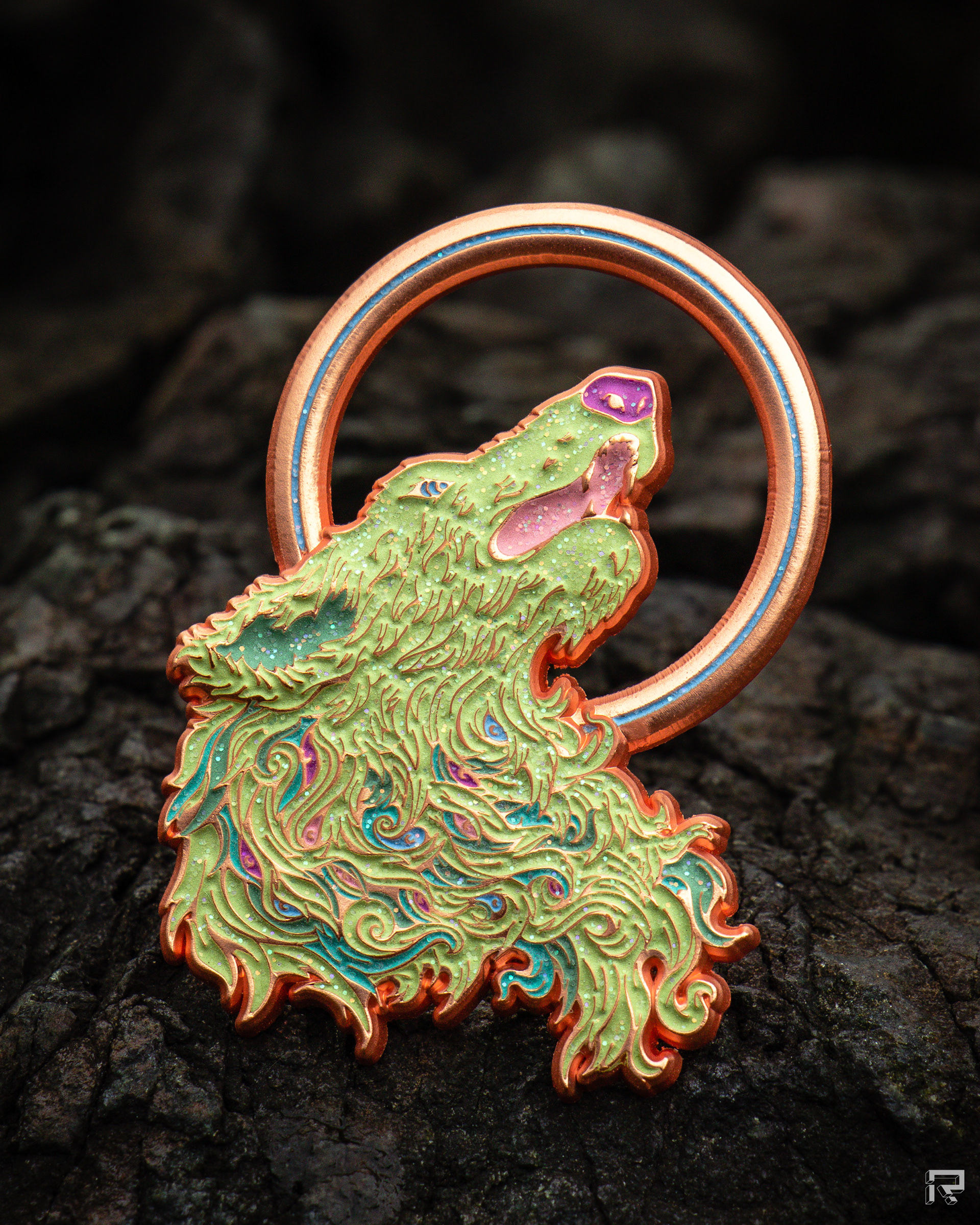 Enamel pin featuring artwork of a wolf's head howling at a ring-shaped moon. The wolf's fur undulates with a flame-like quality, the line work is highly detailed. The wolf's head is light green, with an orange mouth and teal areas to indicate shadows.. The pin is made of copper metal.