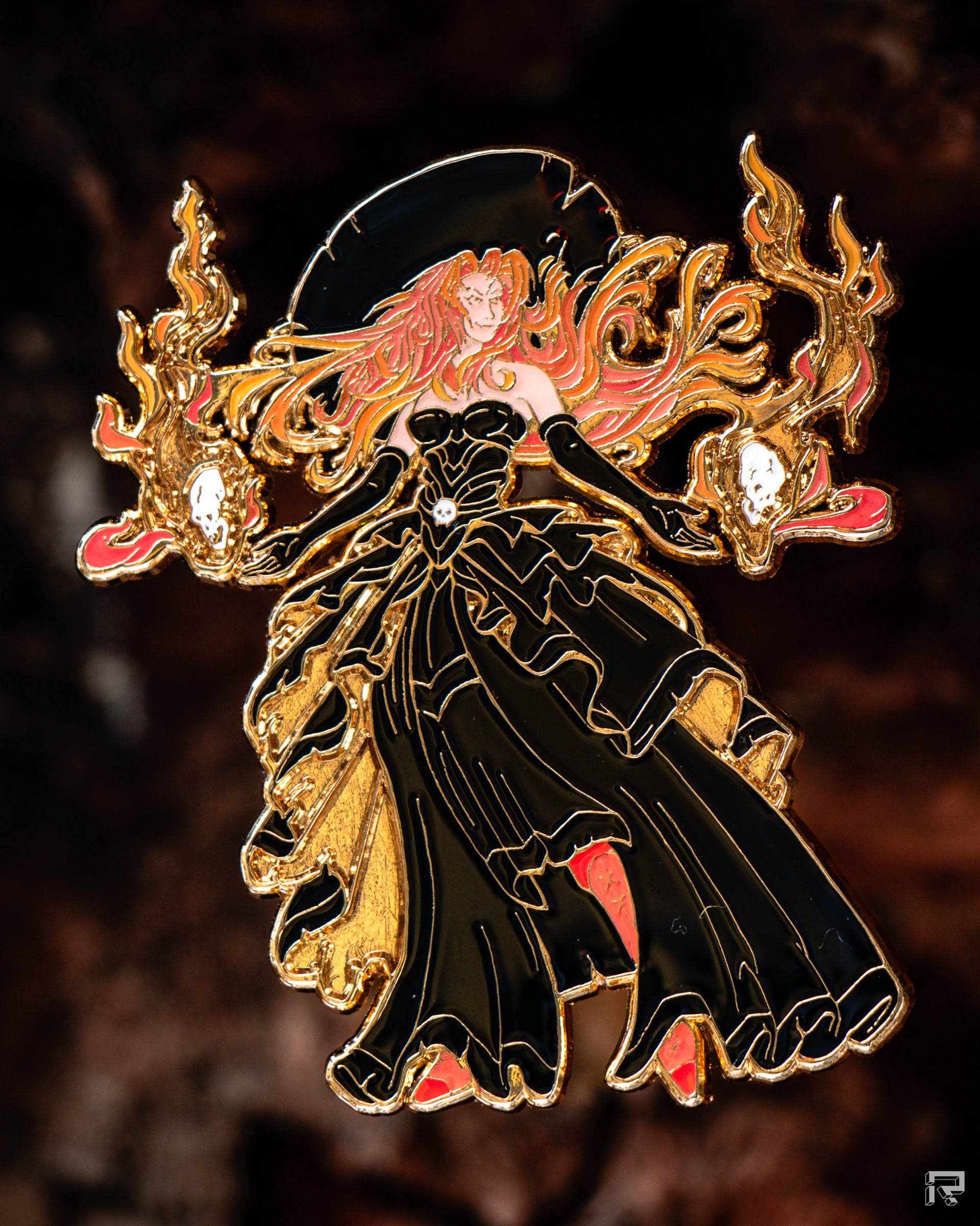 Enamel pin of a beautiful enchantress, long billowing black dress, two skulls with flames float above either hand, dynamic flowing red hair, gold metal