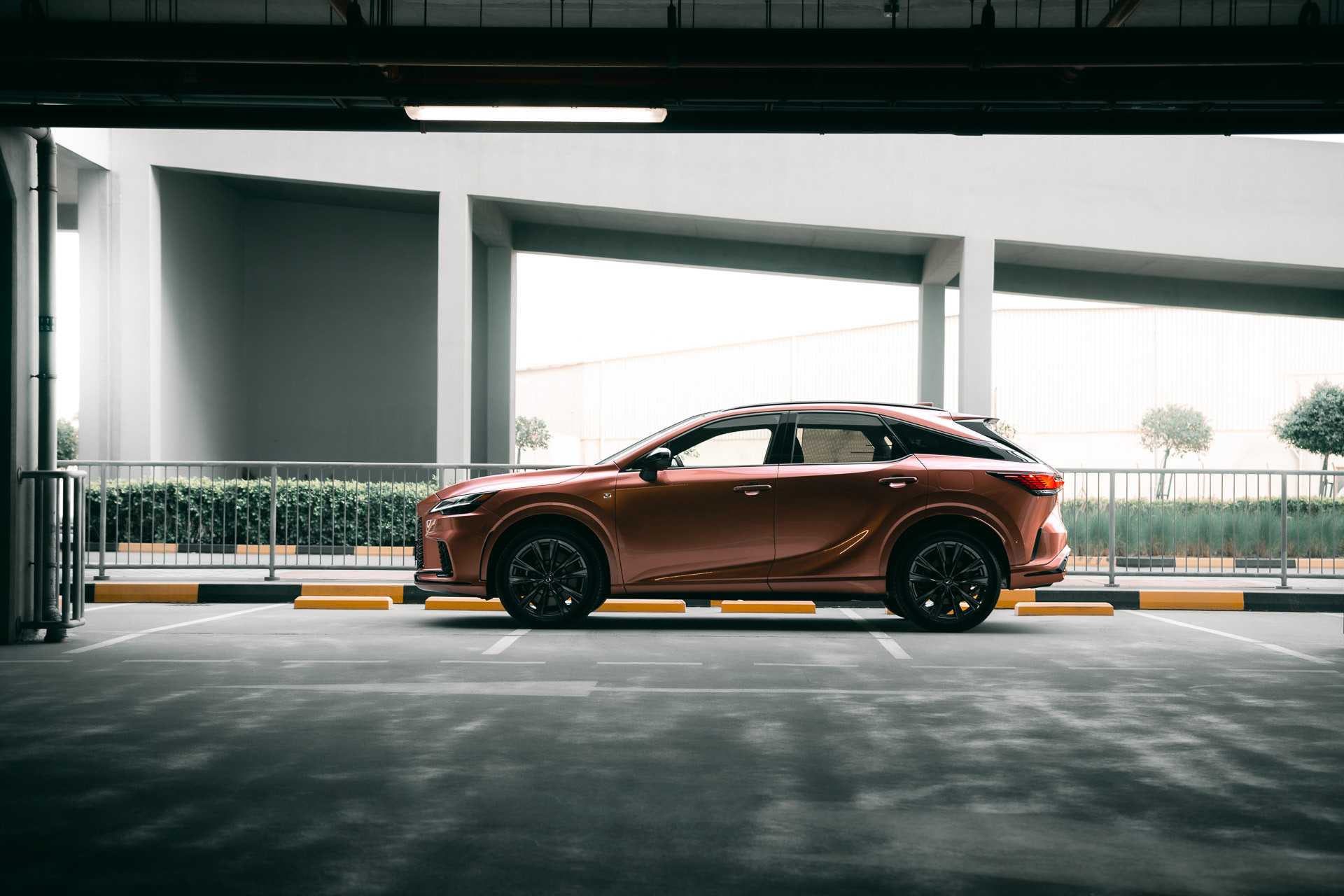 Side profile of the Lexus RX500h F SPORT in copper, parked in a clean modern parking structure in Bahrain.