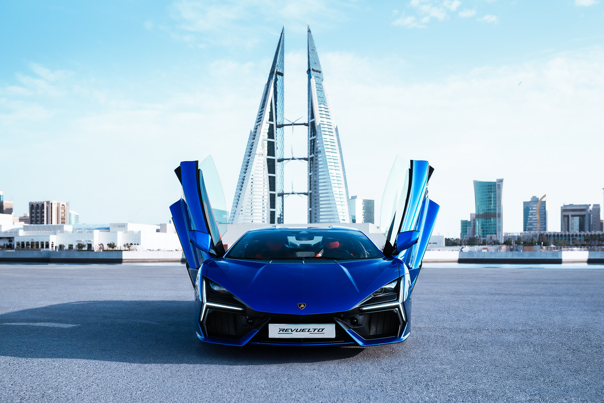 Blue Lamborghini Revuelto front view with both scissor doors open, Bahrain World Trade Center in the background, Manama