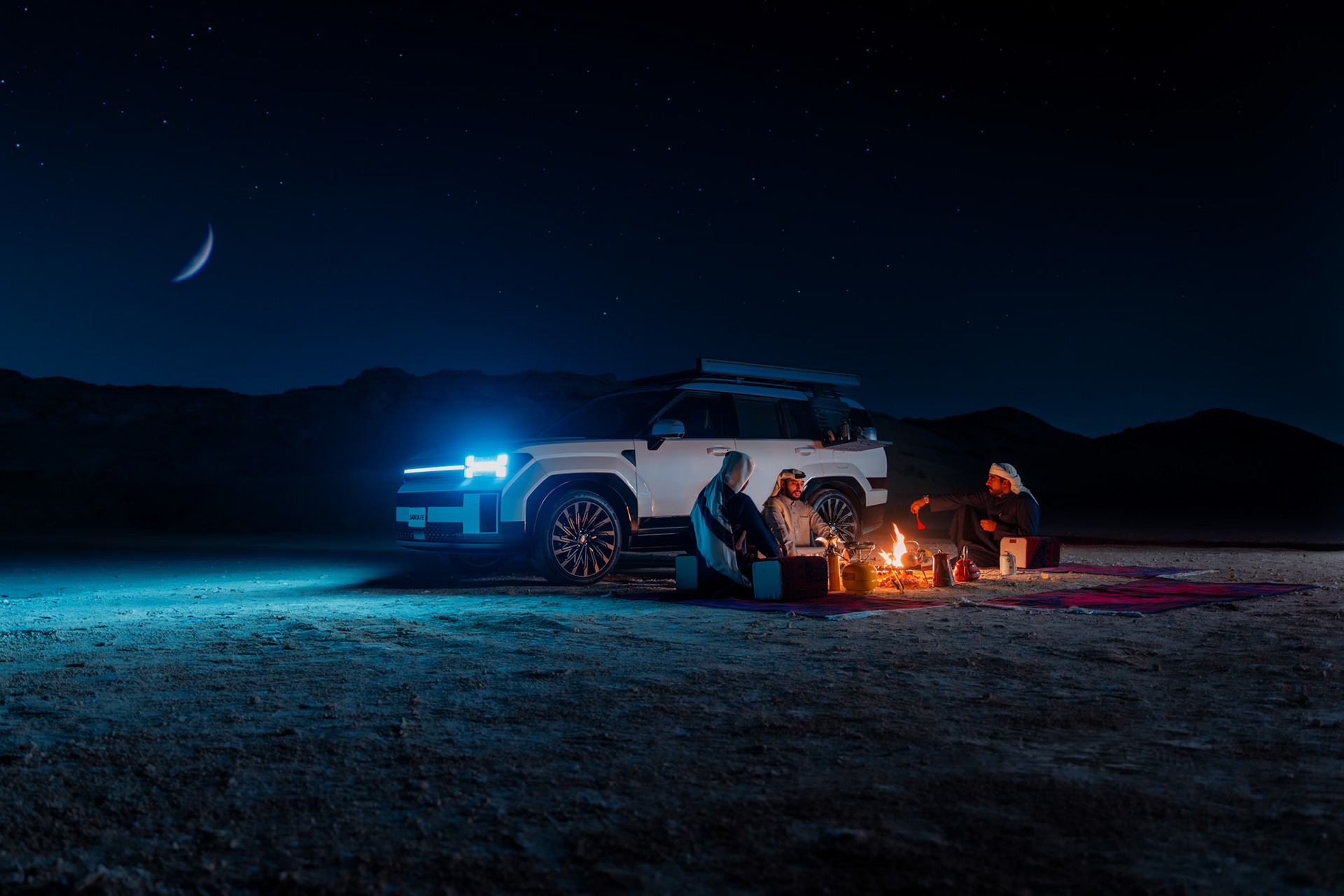 HYUNDAI SANTA FE under a starlit desert sky with crescent moon, headlights on beside the group's campfire, Bahrain — Shift Mootark