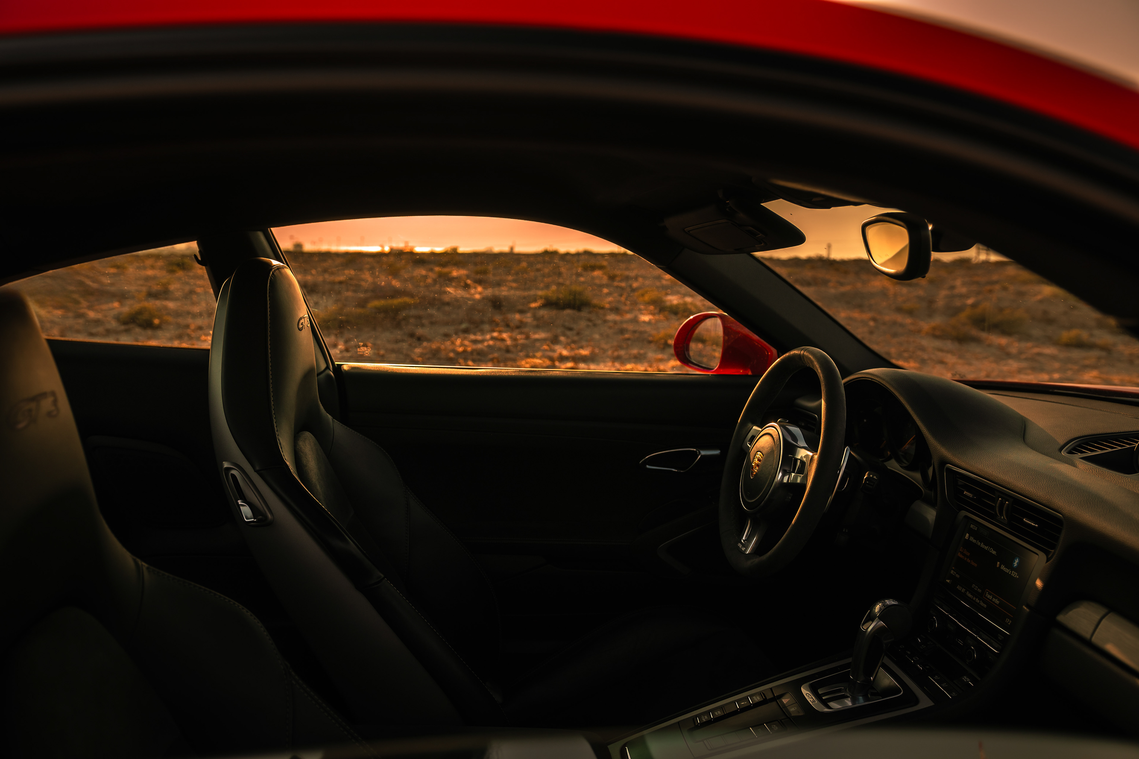 Interior of Porsche 911 GT3 at sunset, steering wheel and seat with desert outside the window