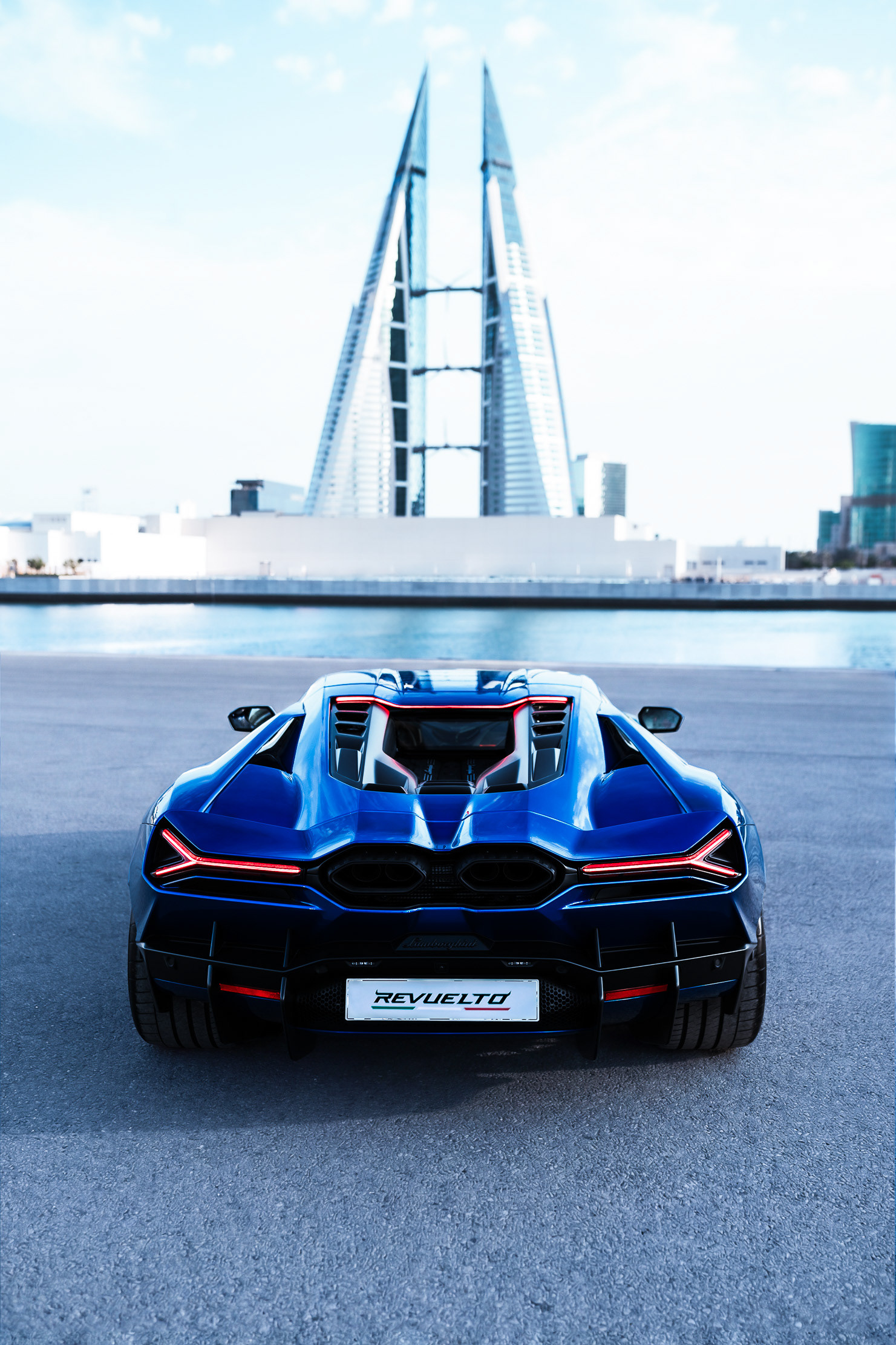 Lamborghini Revuelto rear view with taillights lit, Bahrain Bay towers behind, Manama