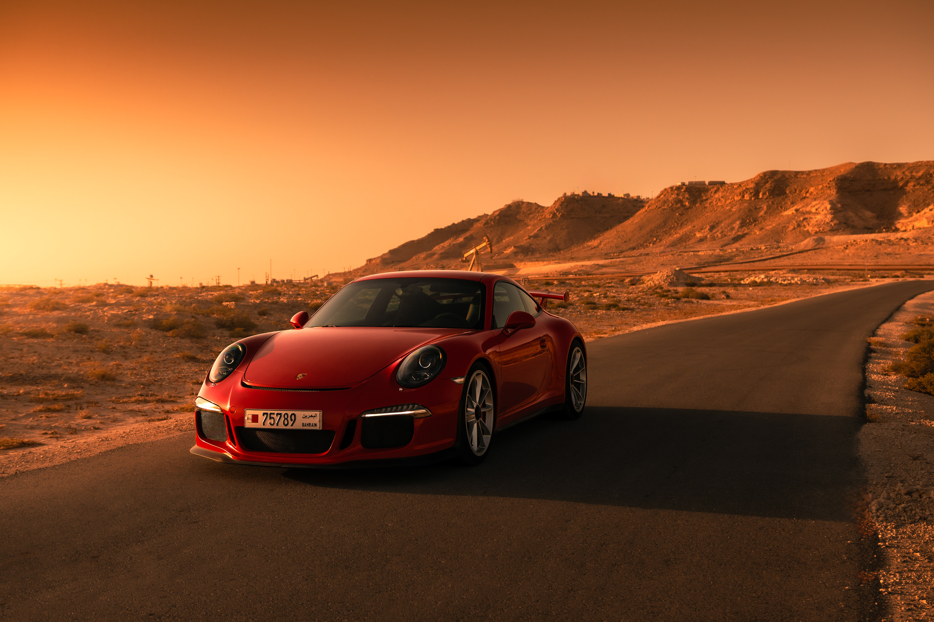 Red Porsche 911 GT3 front three‑quarter on a desert road with sunset hills