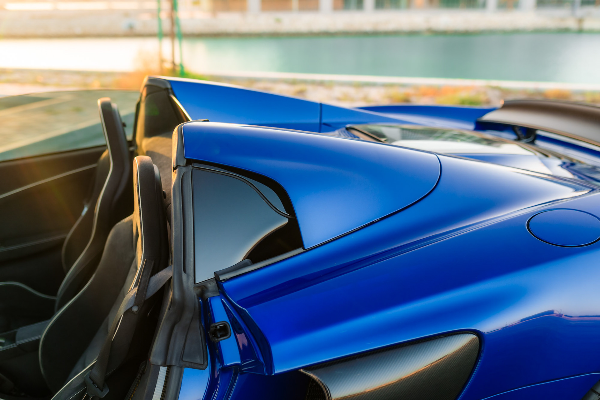 McLaren 650S Spider roof and rear section in Bahrain, showing the convertible top mechanism and sculpted blue bodywork under golden-hour light.