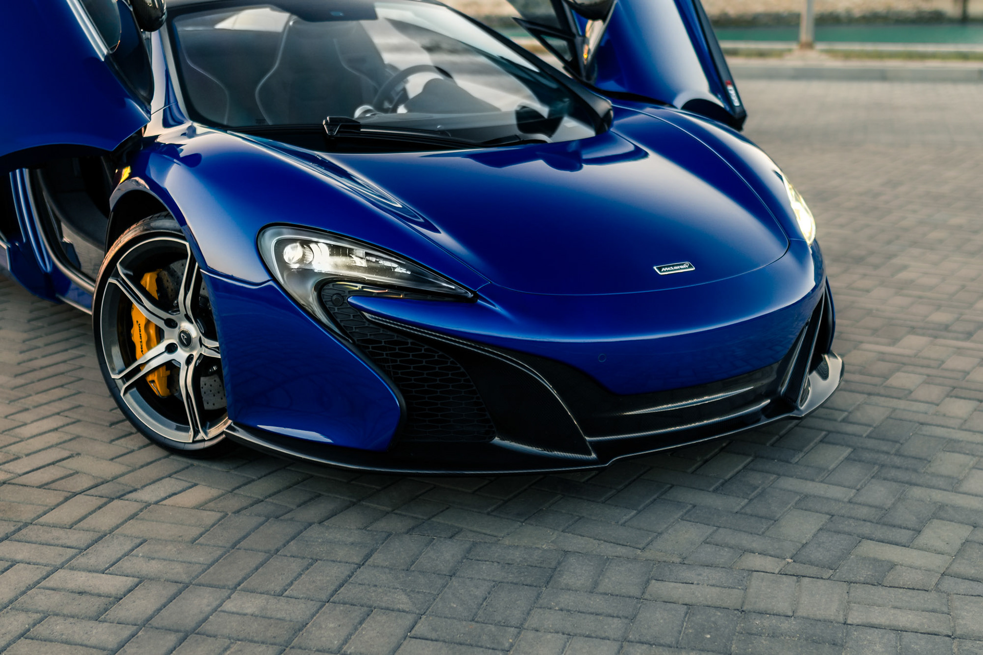 Front three-quarter close-up of the McLaren 650S Spider in Bahrain showing the headlight, front splitter, and yellow brake caliper under warm evening light