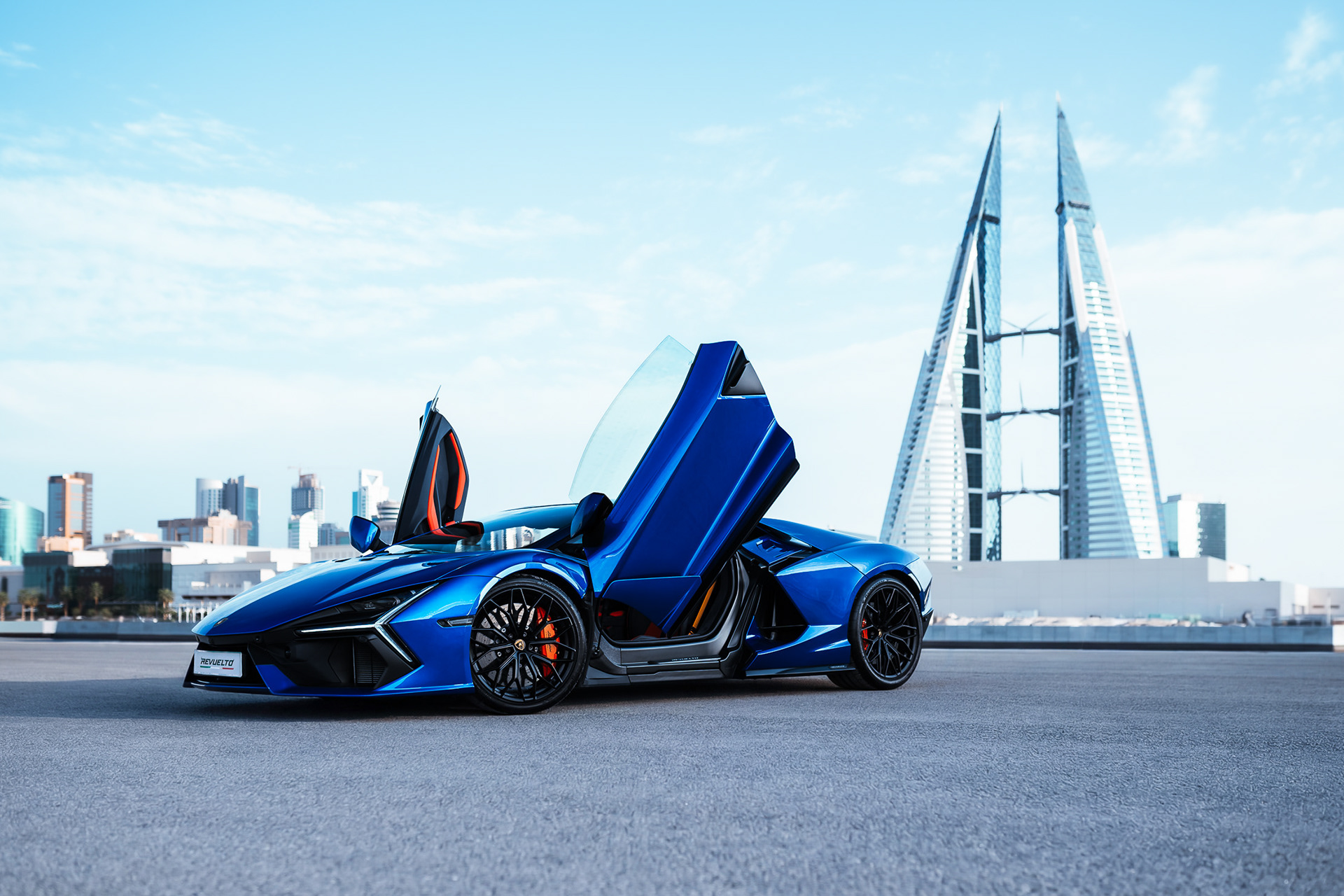 Lamborghini Revuelto with vertical doors raised, front three-quarter view against the Bahrain Bay towers in Manama, Bahrain