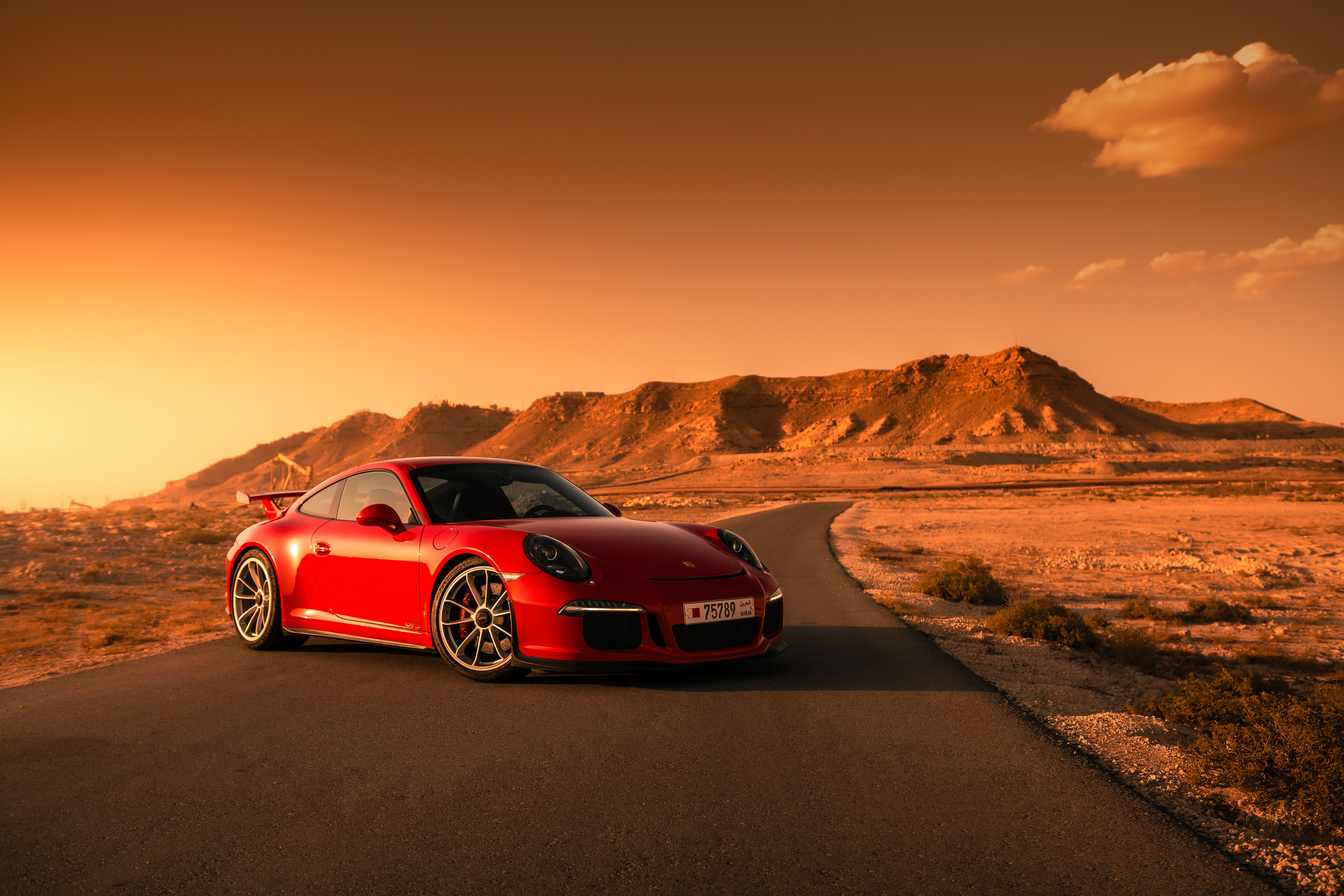 Porsche 911 GT3 front three‑quarter in golden desert light with mountains and curving road behind