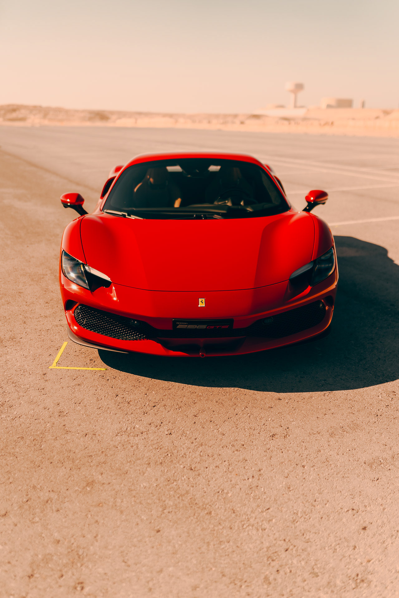 Front view of a red Ferrari 296 GTS parked on set under desert sunlight in Sakhir, Bahrain, captured during the Ferrari × Shell commercial production.