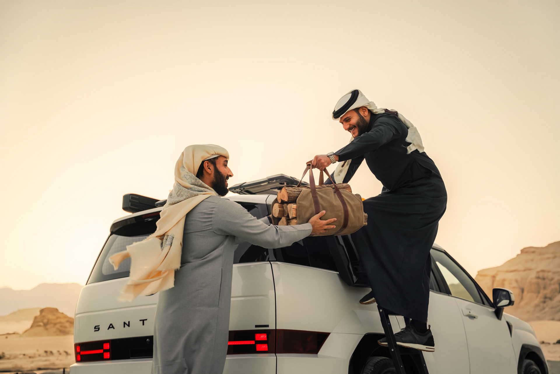 HYUNDAI SANTA FE roof rack loading with cargo box and duffel bag, desert rock formations backdrop, Bahrain — Shift Mootark