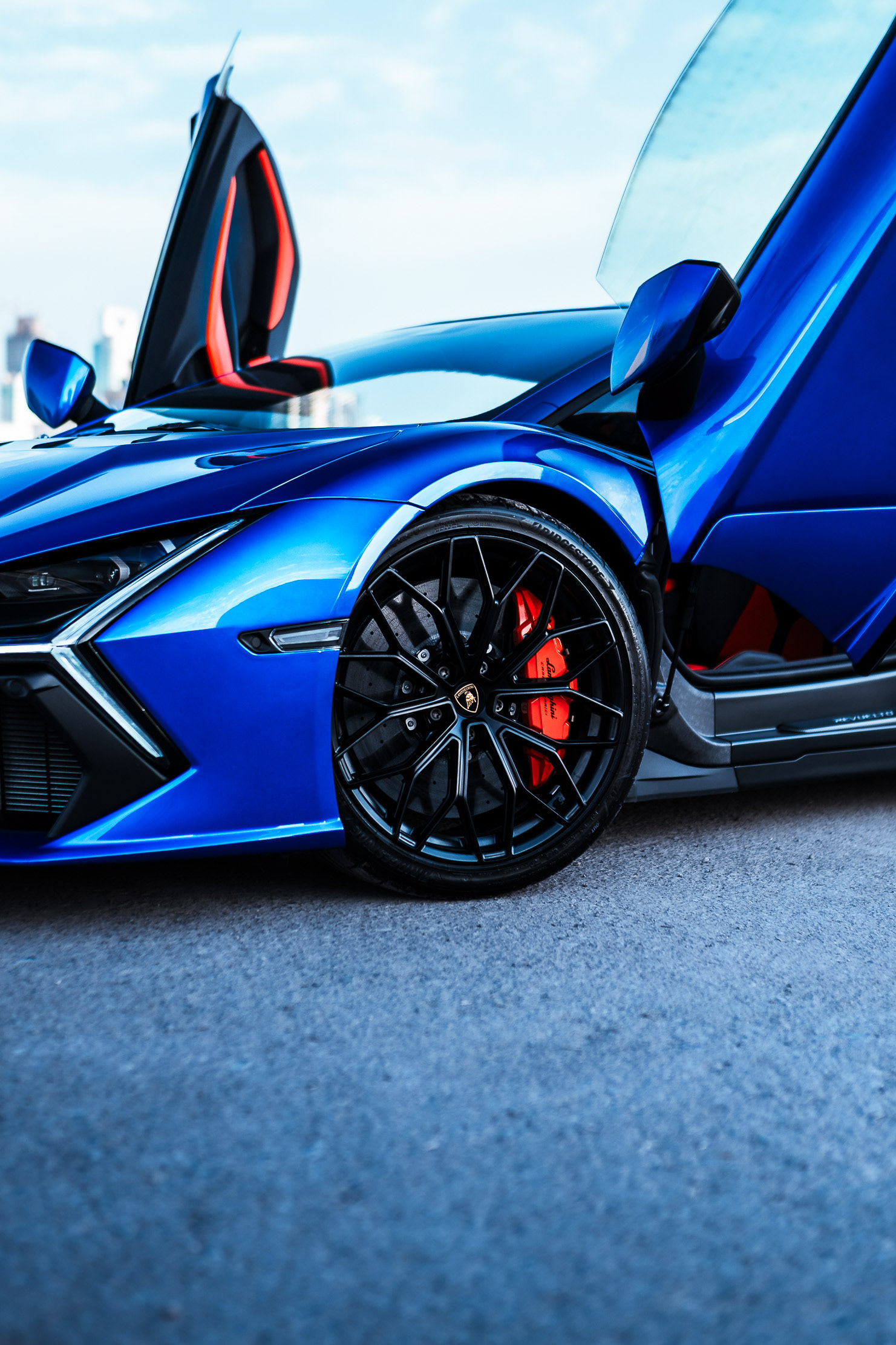 Lamborghini Revuelto front quarter view with scissor door raised, red brake calipers visible