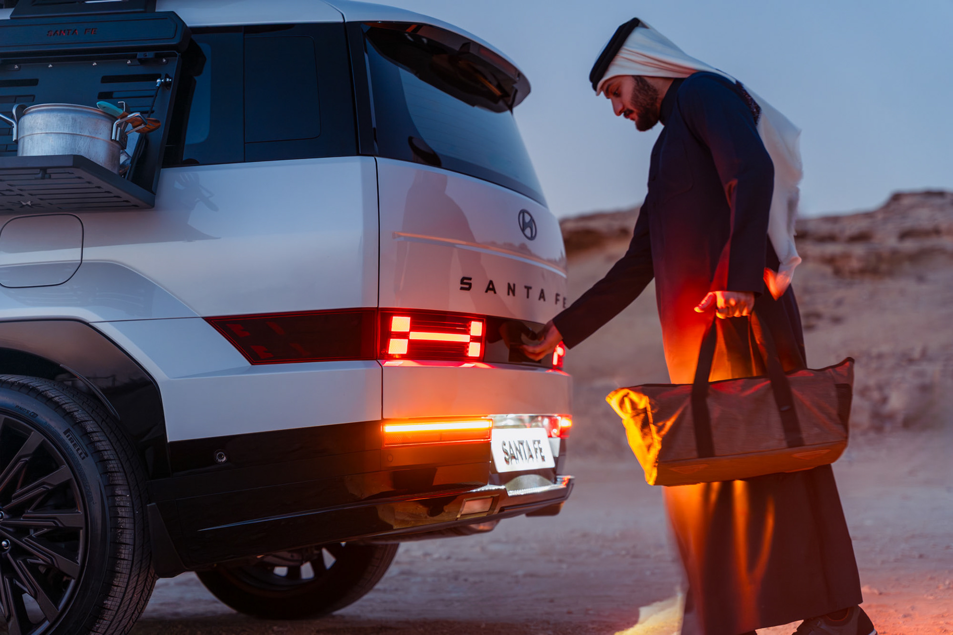 HYUNDAI SANTA FE open tailgate close-up with man loading a duffel bag, warm sunset light, Bahrain — Shift Mootark