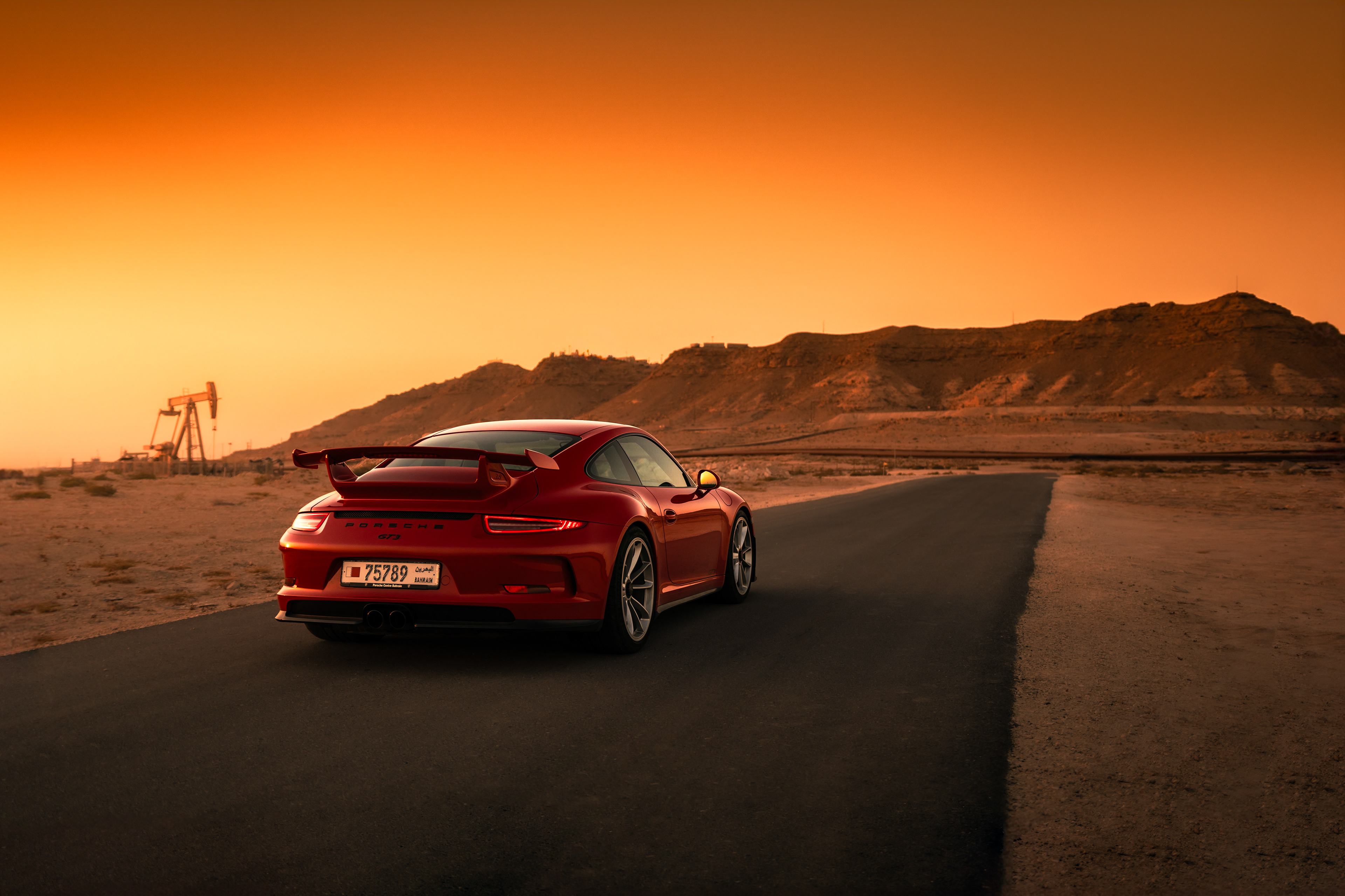 Rear three‑quarter of Porsche 911 GT3 on a desert road at golden hour with hills in the distance.