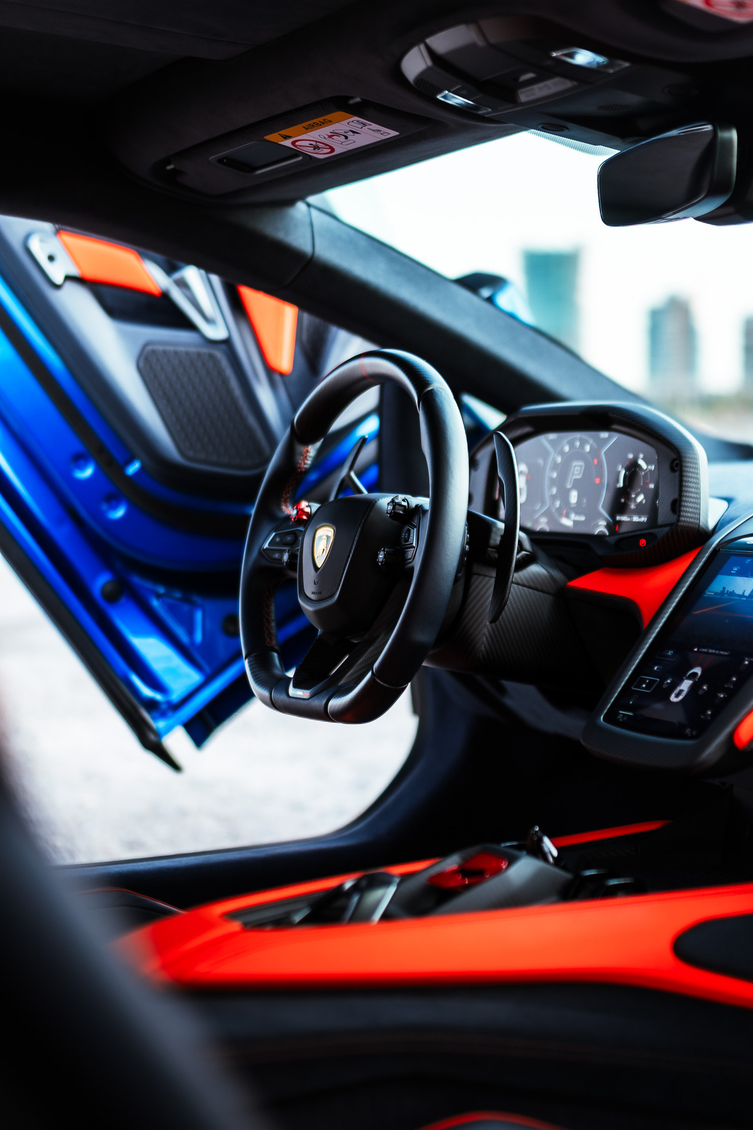 Lamborghini Revuelto cockpit interior showing the steering wheel, digital gauge cluster, and red and blue Alcantara trim