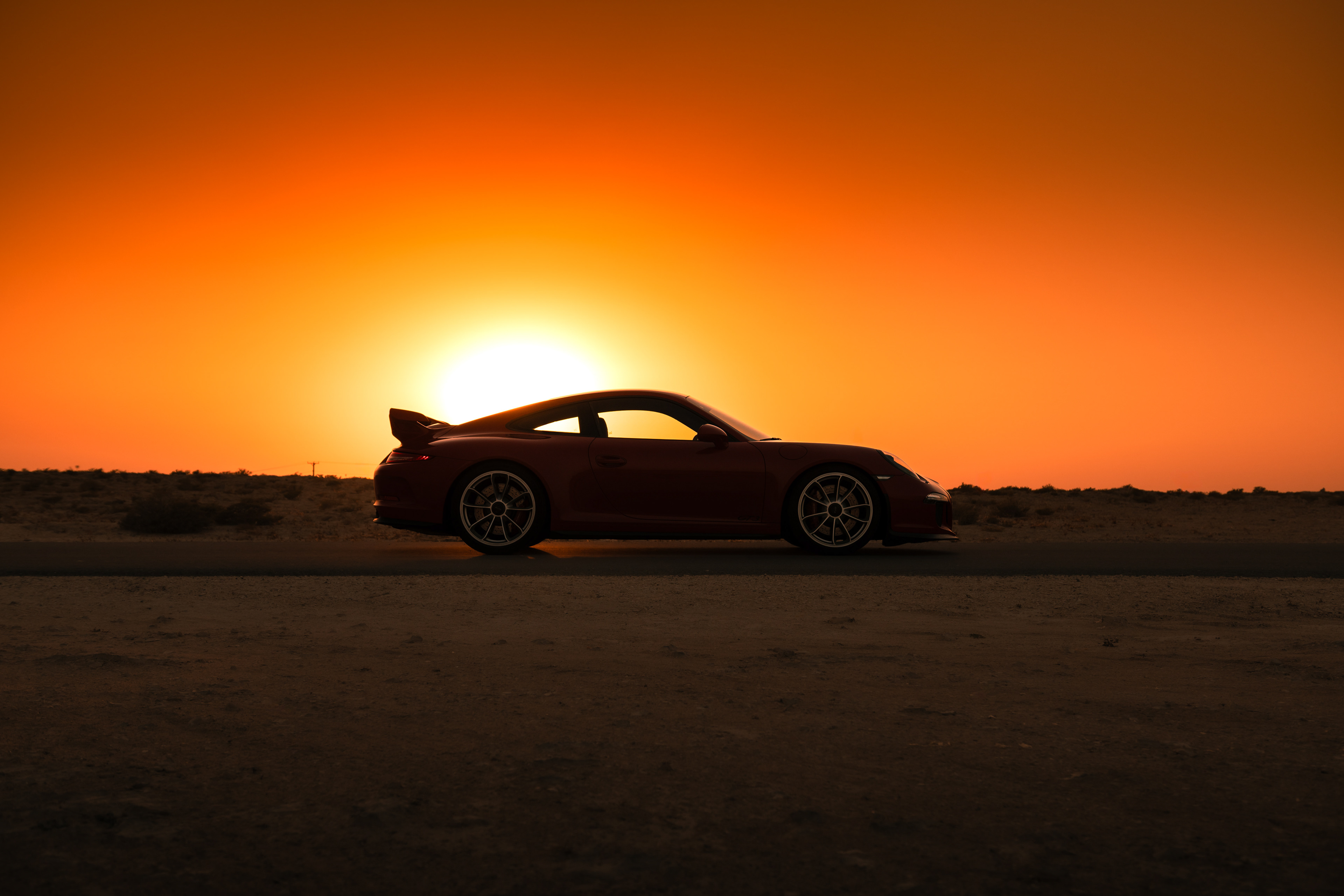 Silhouette of red Porsche 911 GT3 with rear wing against a desert sunset horizon.