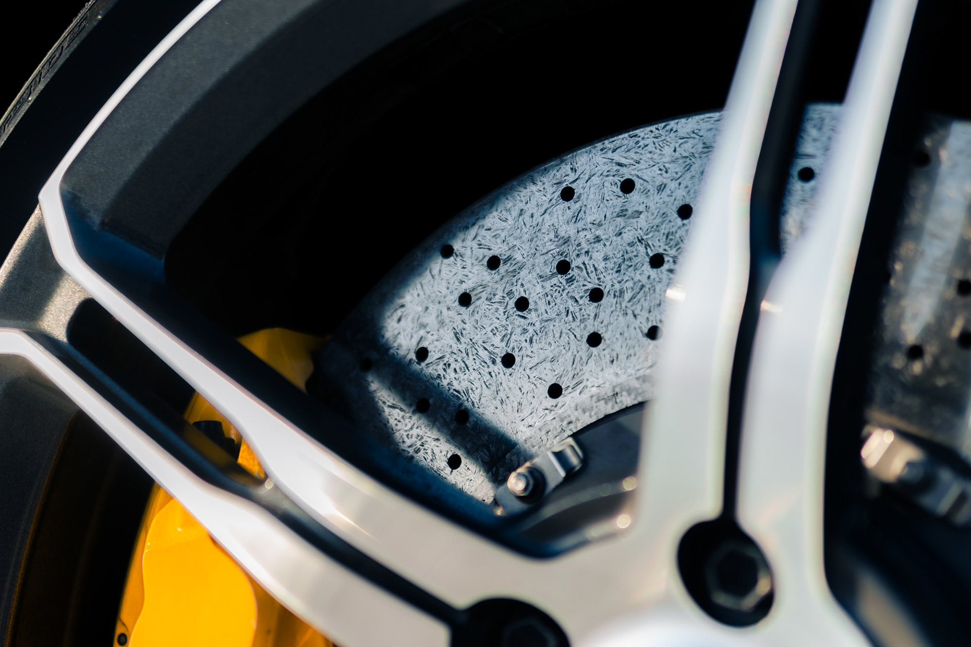 Close-up of the McLaren 650S Spider carbon-ceramic brake disc and yellow caliper showing the detailed surface texture and wheel spokes