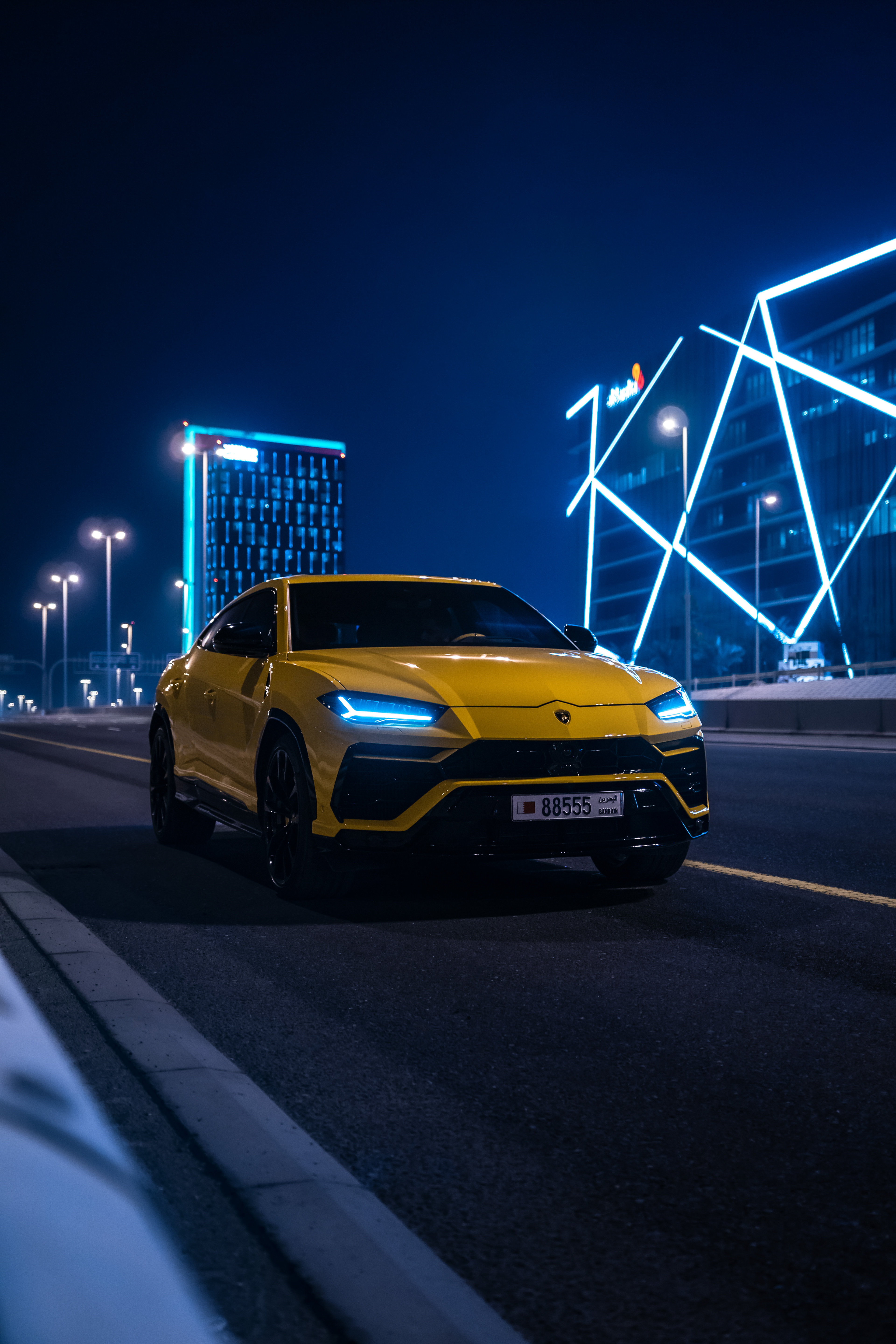 Yellow Lamborghini Urus at night in Bahrain Bay with blue neon buildings and street lights
