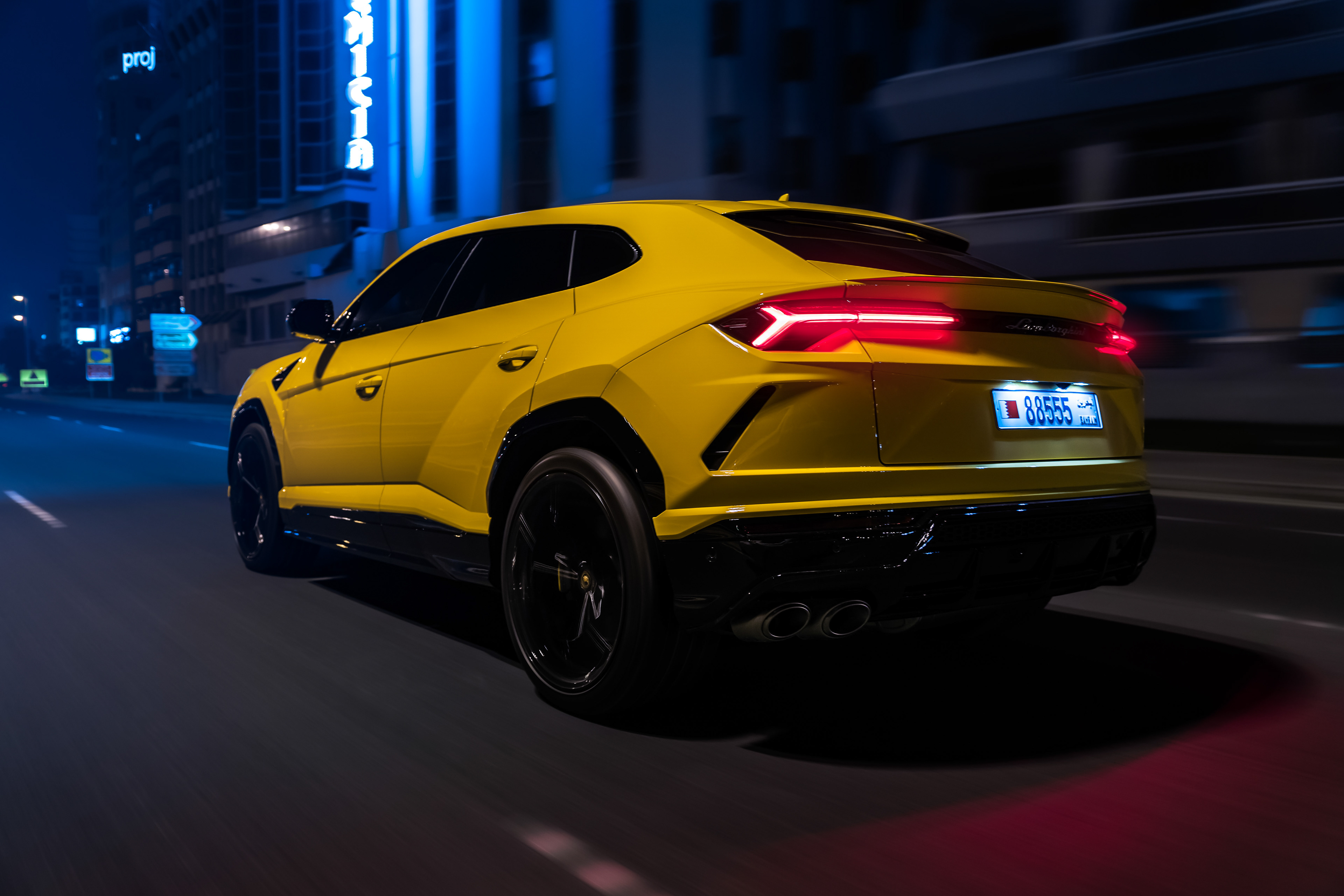 Yellow Lamborghini Urus driving through Bahrain city streets at night with blue neon lights in the background