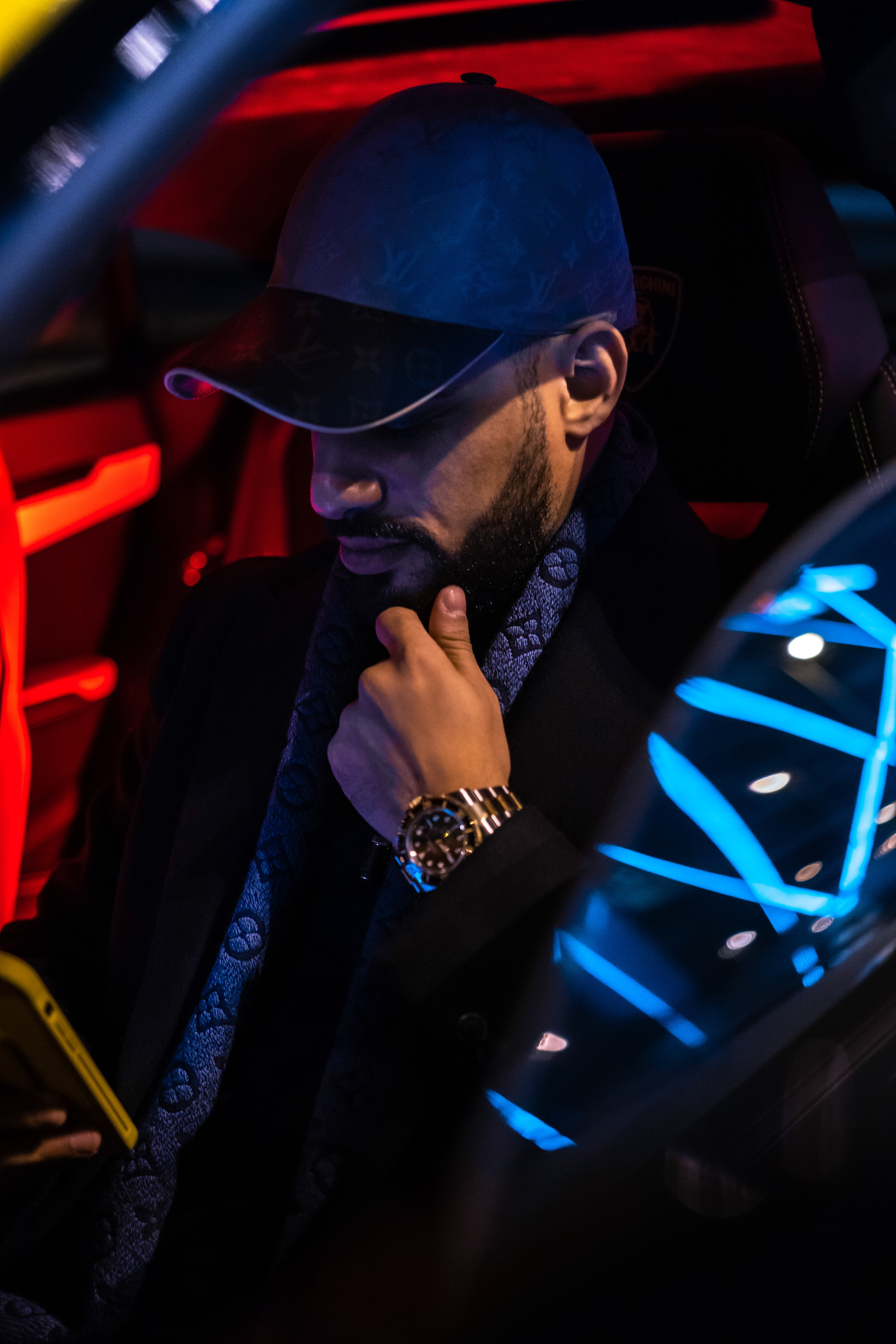 Lifestyle details beside a Lamborghini Urus—LV scarf, gold Rolex, and Lamborghini seat crest under red interior light